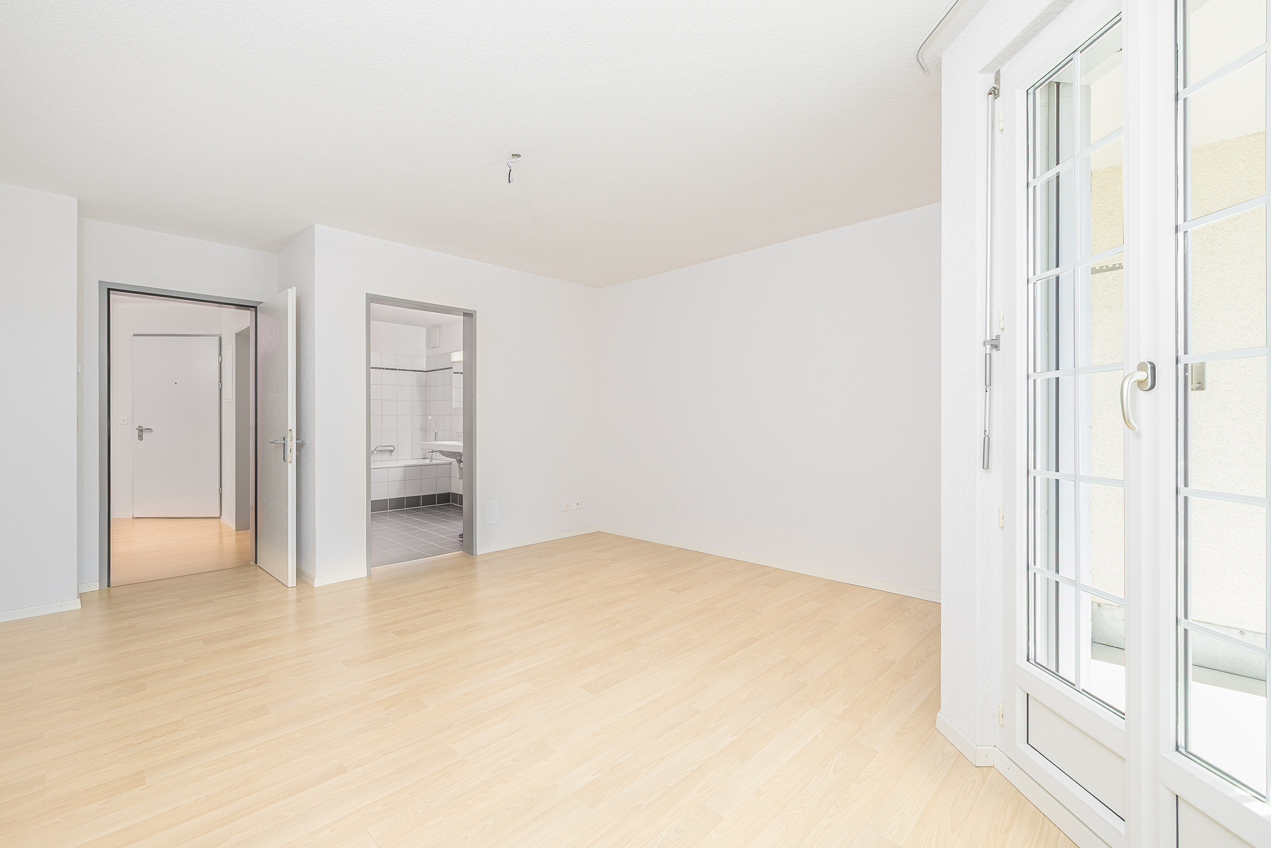 Heller leerer Wohnraum mit Blick ins Badezimmer und Flügeltür zur Terrasse