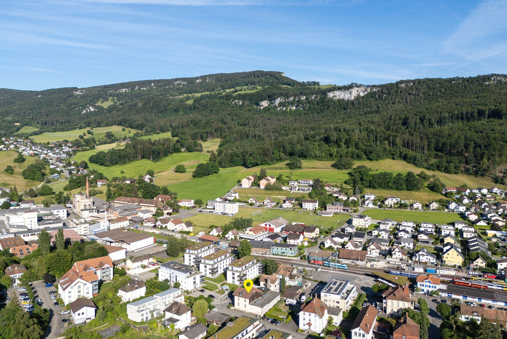 Luftaufnahme einer Ortschaft im Tal vor bewaldeten Bergen