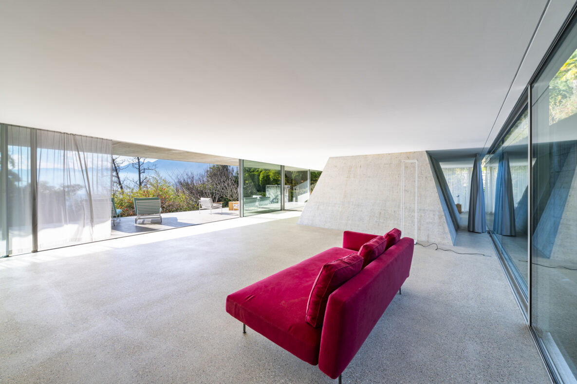 Großer, minimalistischer Wohnraum mit Panoramafenstern und rotem Sofa