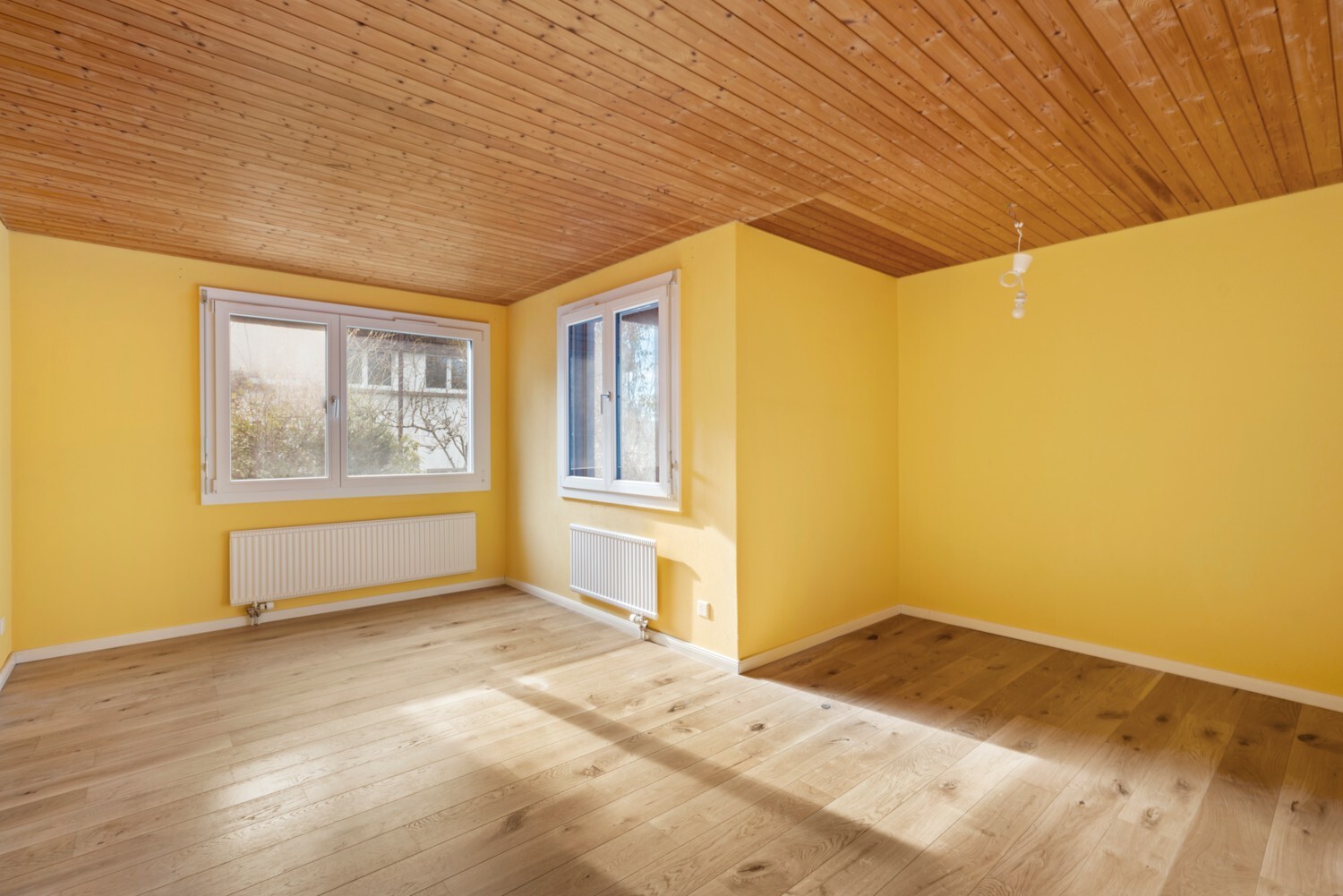 Helles, leerstehendes Zimmer mit Holzdecke und gelben Wänden