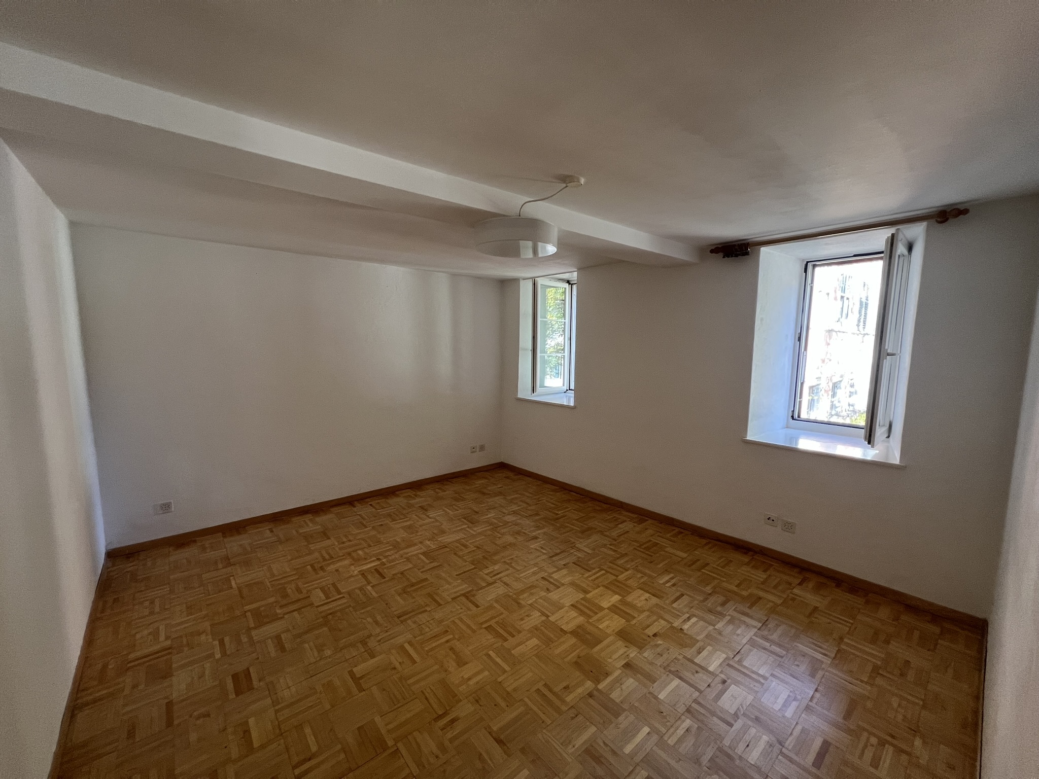 Leerer Wohnraum mit Parkett und zwei Fenstern