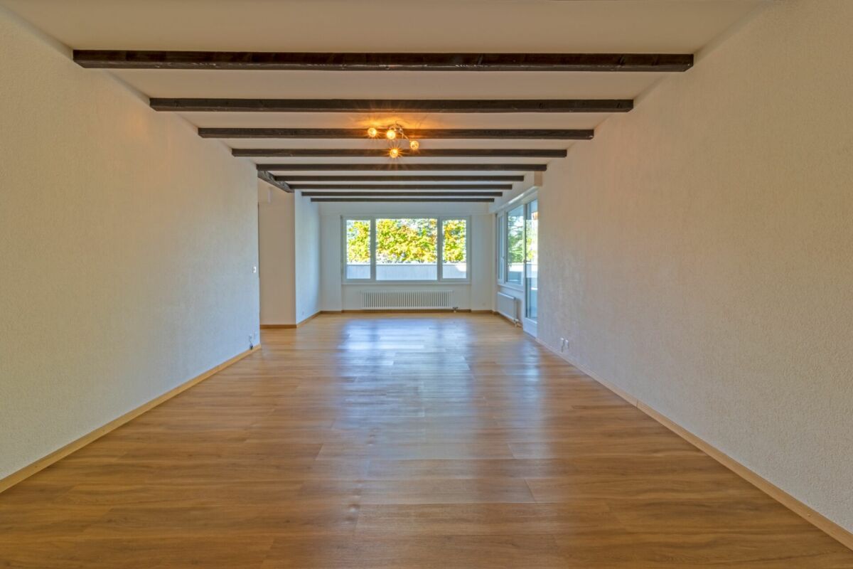 Langer heller Wohnraum mit Holzbalken und großen Fenstern