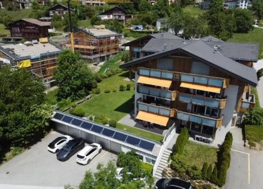 Luftaufnahme eines alpinen Mehrfamilienhauses mit Terrassen und Tiefgarage