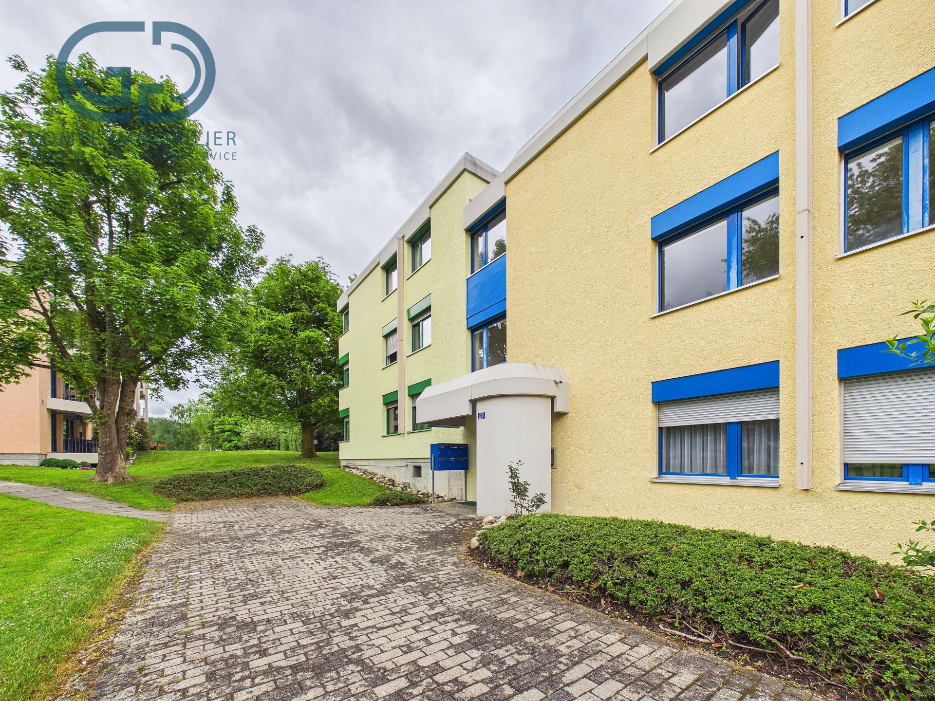 Mehrfamilienhaus mit gelber Fassade und blauen Fensterrahmen