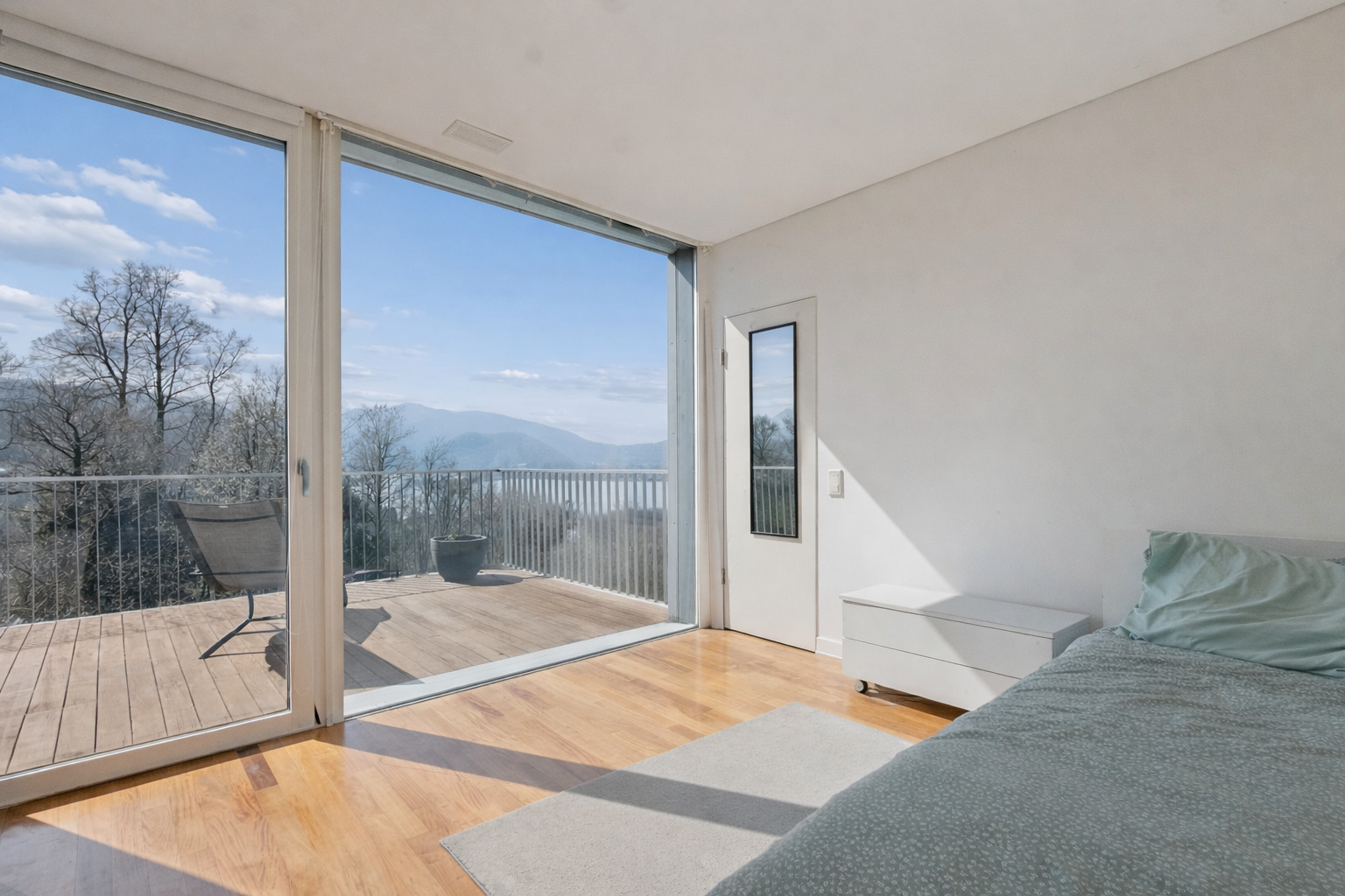 Schlafzimmer mit bodentiefer Glasfront und Balkonblick