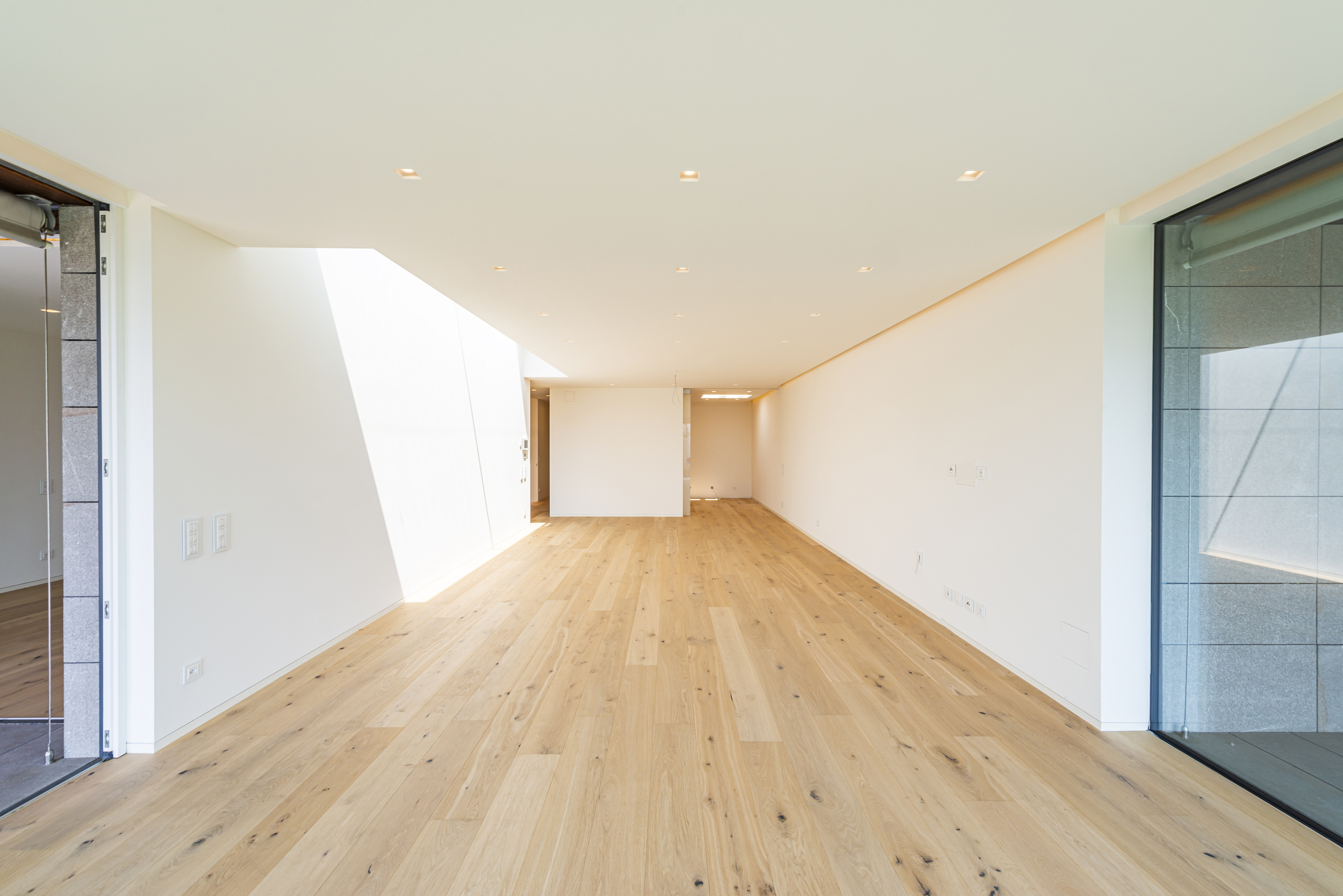 Heller, leerer Wohnraum mit Holzfußboden und großen Fensterflächen