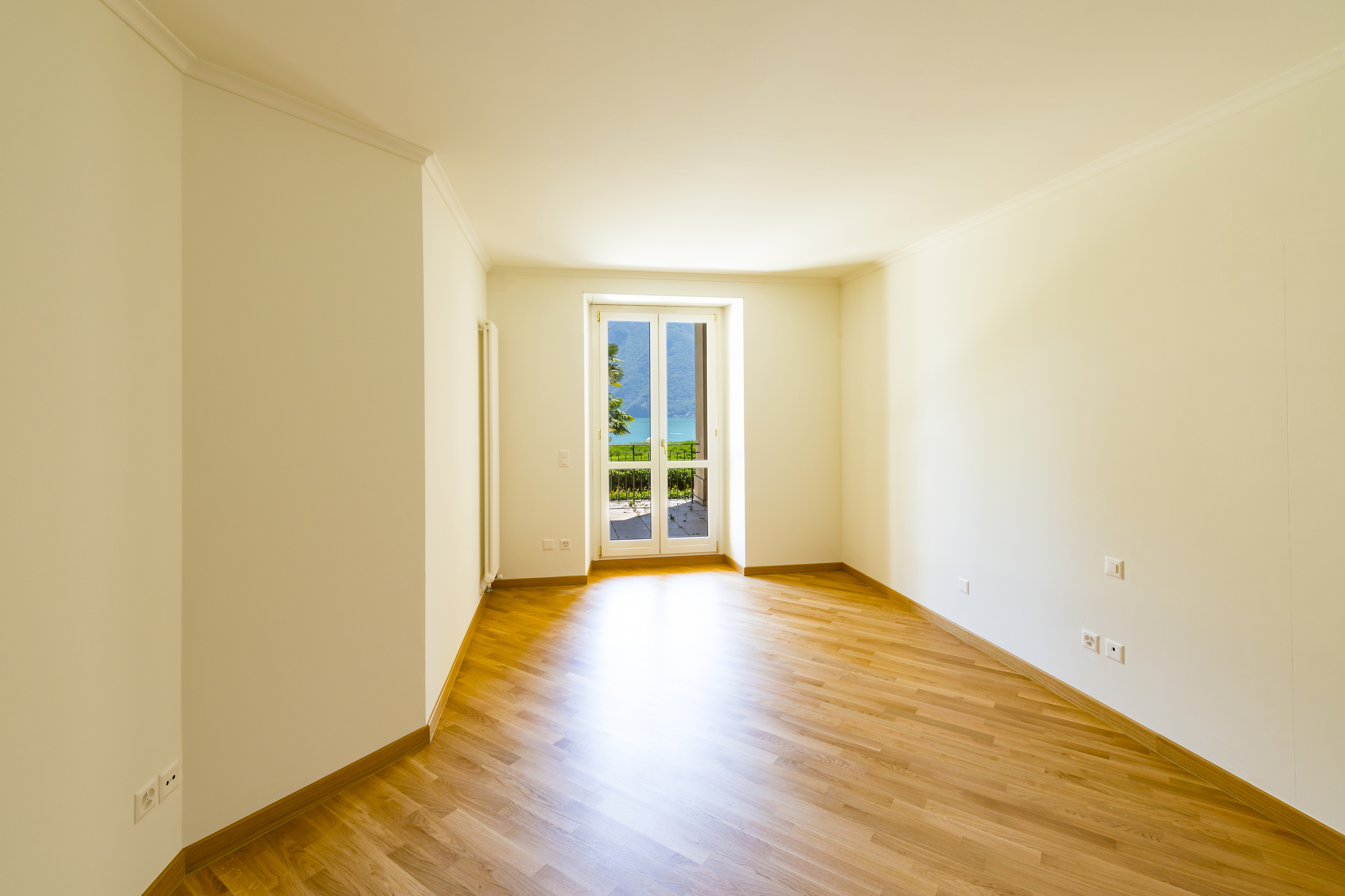 Heller leerer Raum mit Balkon- oder Terrassentür und Ausblick auf Wasser und Berge