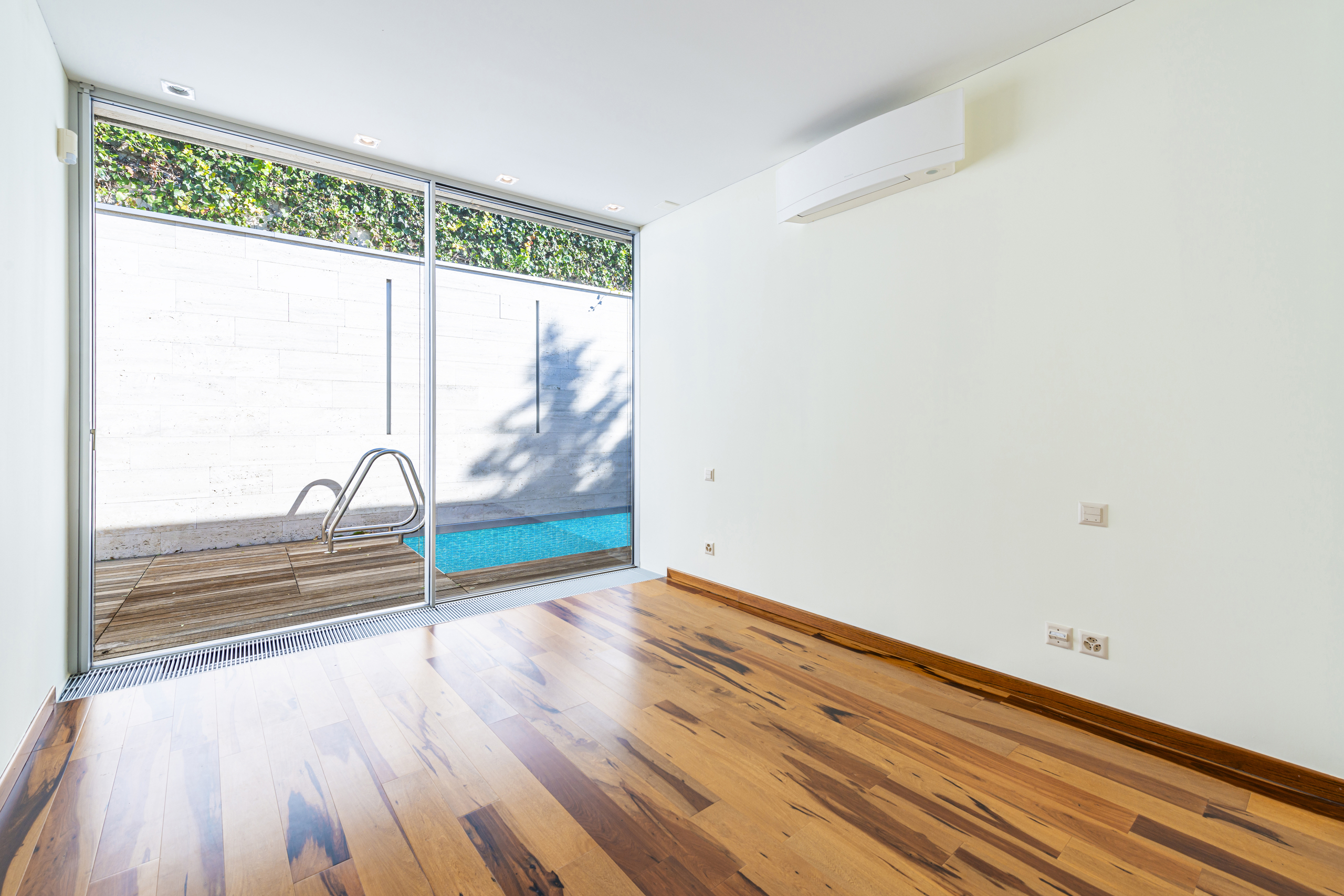 Heller Innenraum mit Holzfußboden und großer Glasfront zum Poolbereich