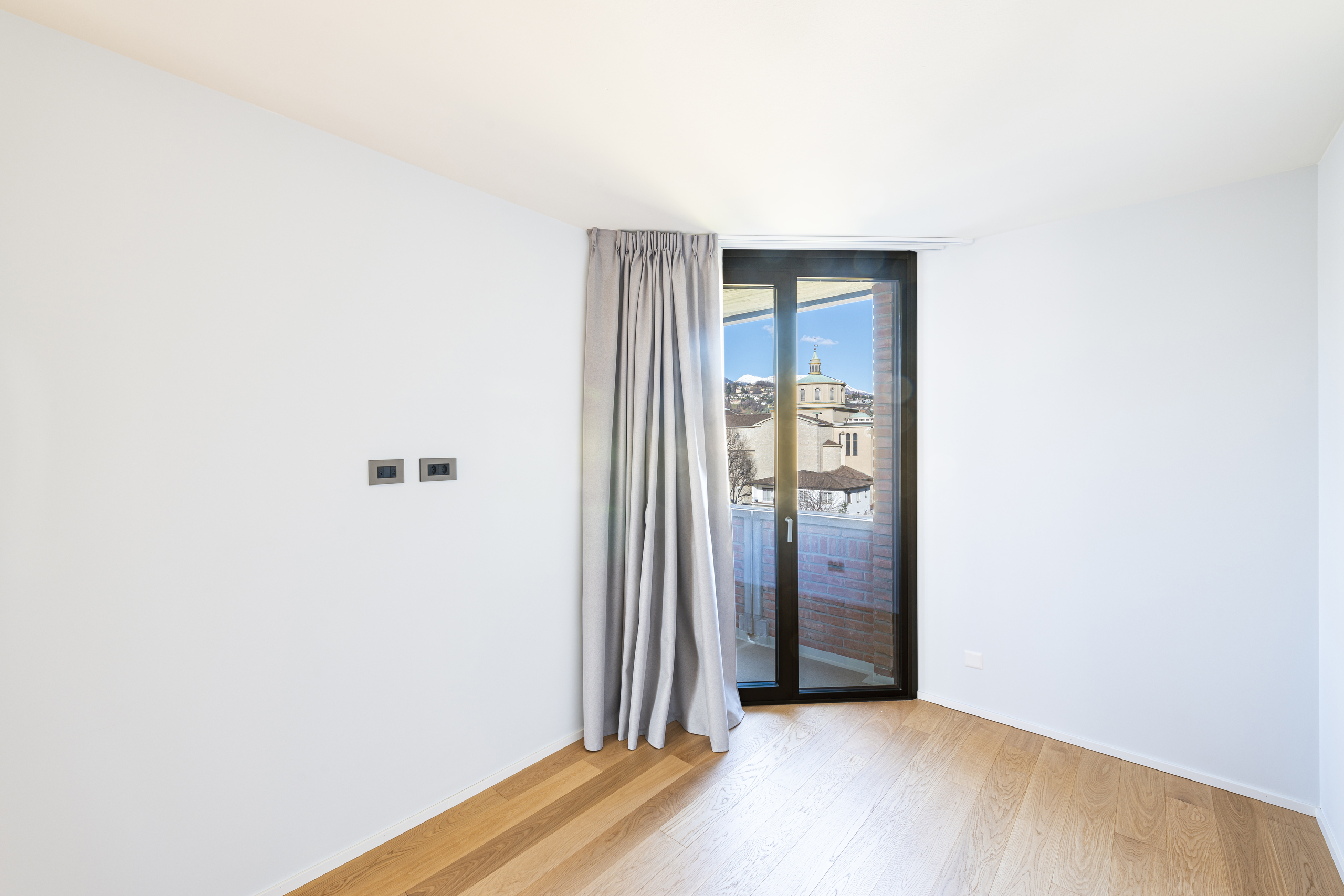 Helles leeres Zimmer mit Balkon und Blick auf eine Kirche