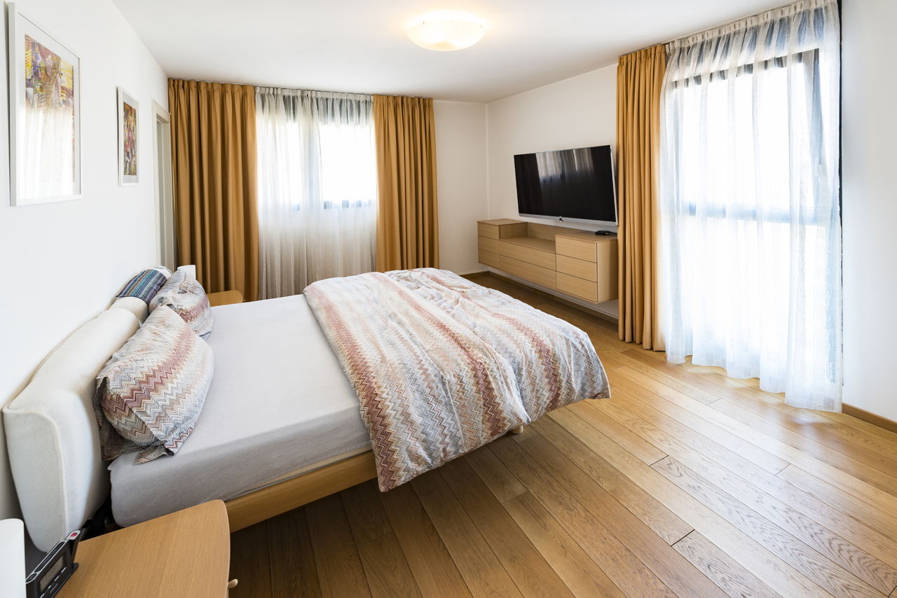 Helles Schlafzimmer mit Bett, TV und großen Fenstern