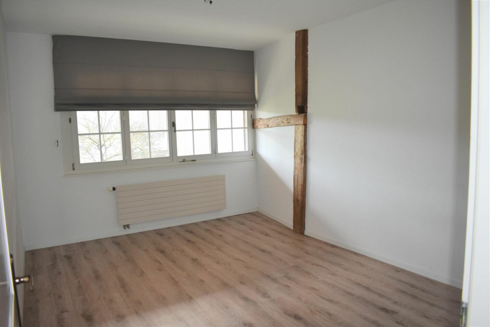 Helles, leeres Zimmer mit Fenster und Holzboden