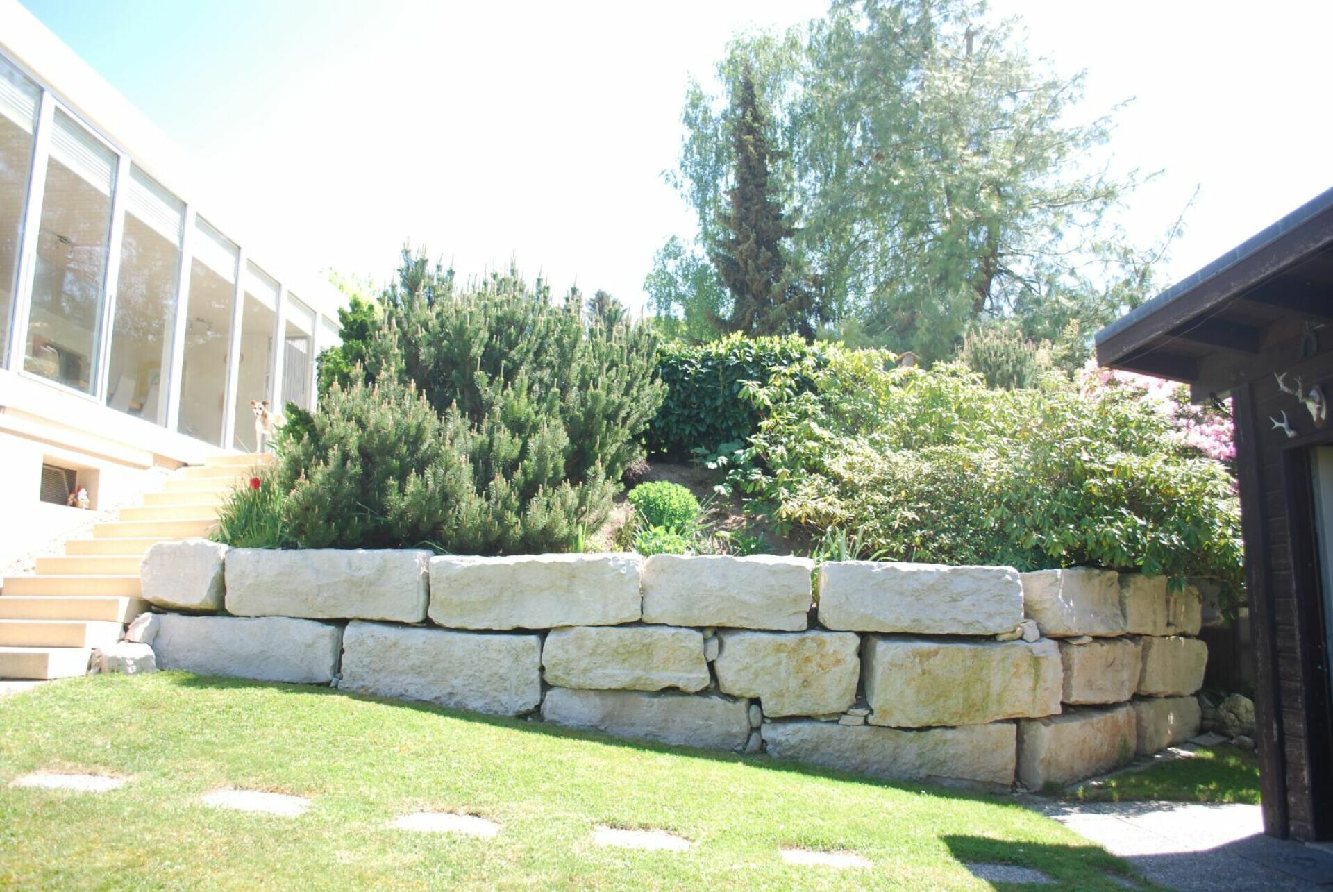 Heller Gartenbereich mit Natursteinmauer und Gebäudeseiten