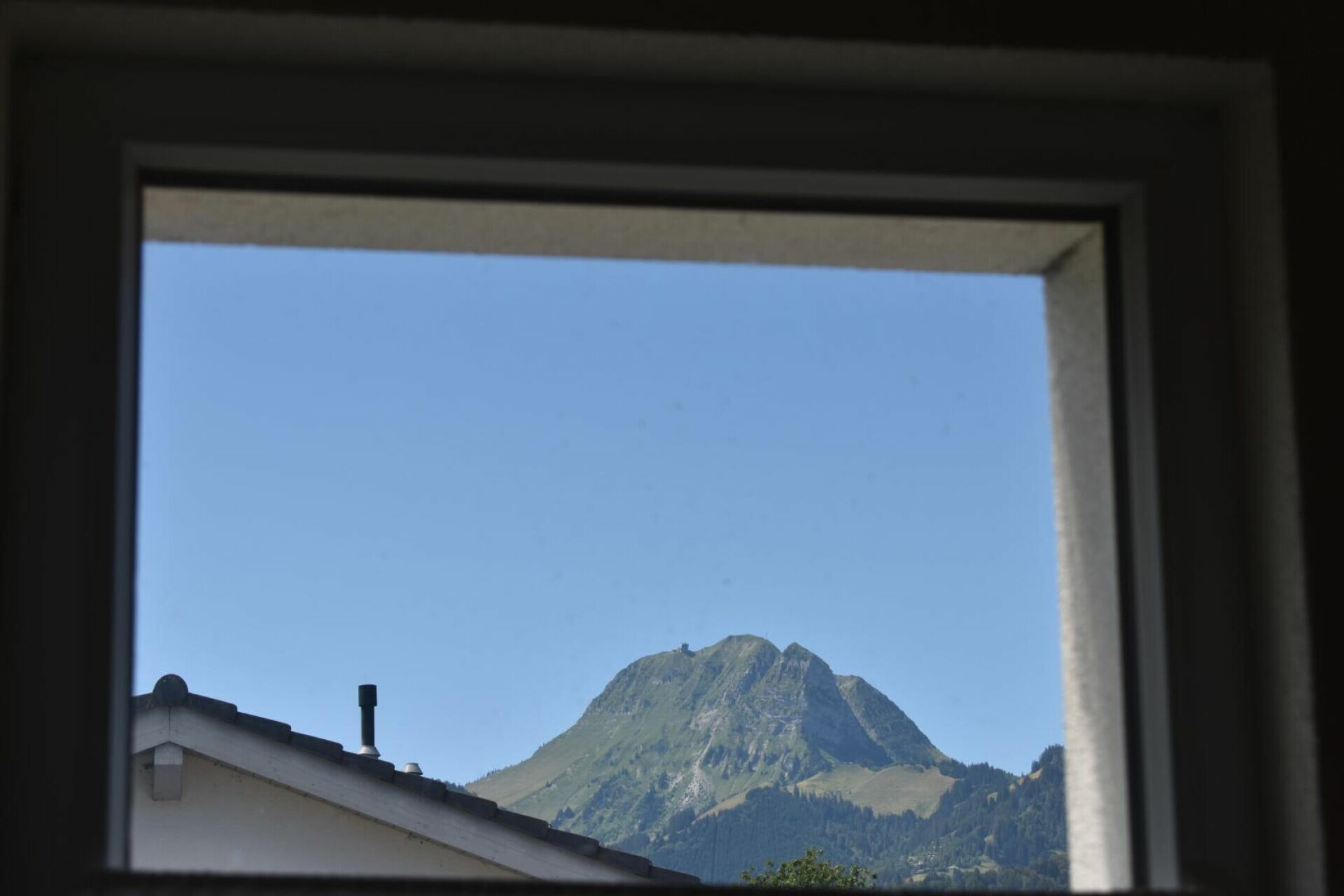 Blick durch ein Fenster auf einen Berg und ein Dach