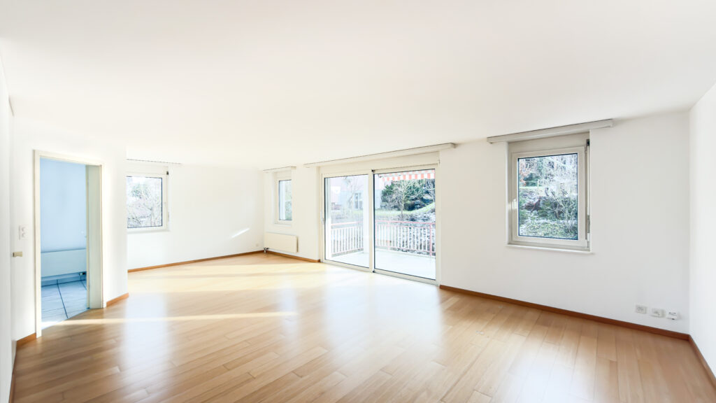 Heller leerer Wohnraum mit großen Fenstern und Balkonzugang