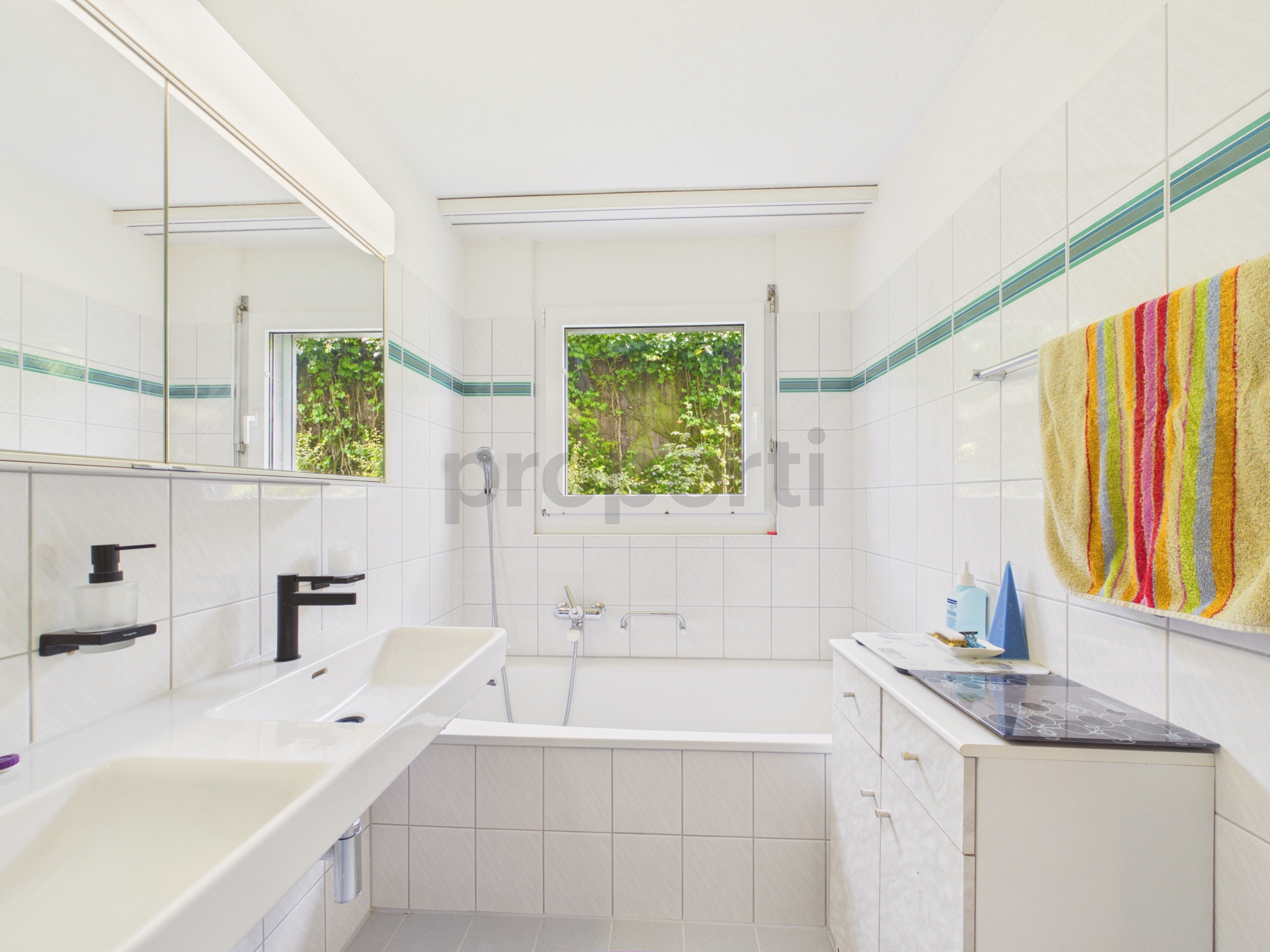 Helles Badezimmer mit Wanne und Fensterblick ins Grüne
