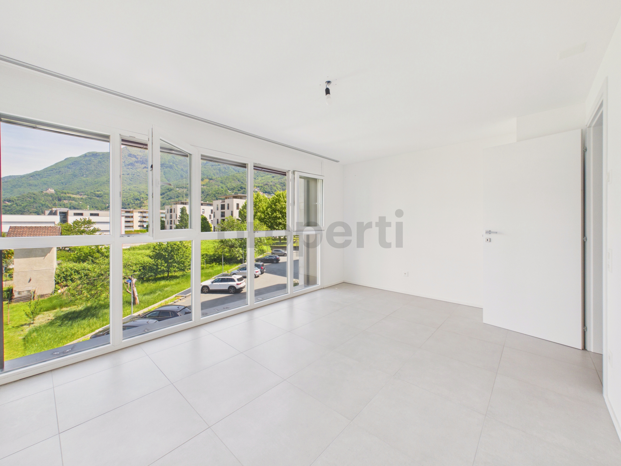 Heller, leerer Wohnraum mit großflächiger Fensterfront und Bergblick