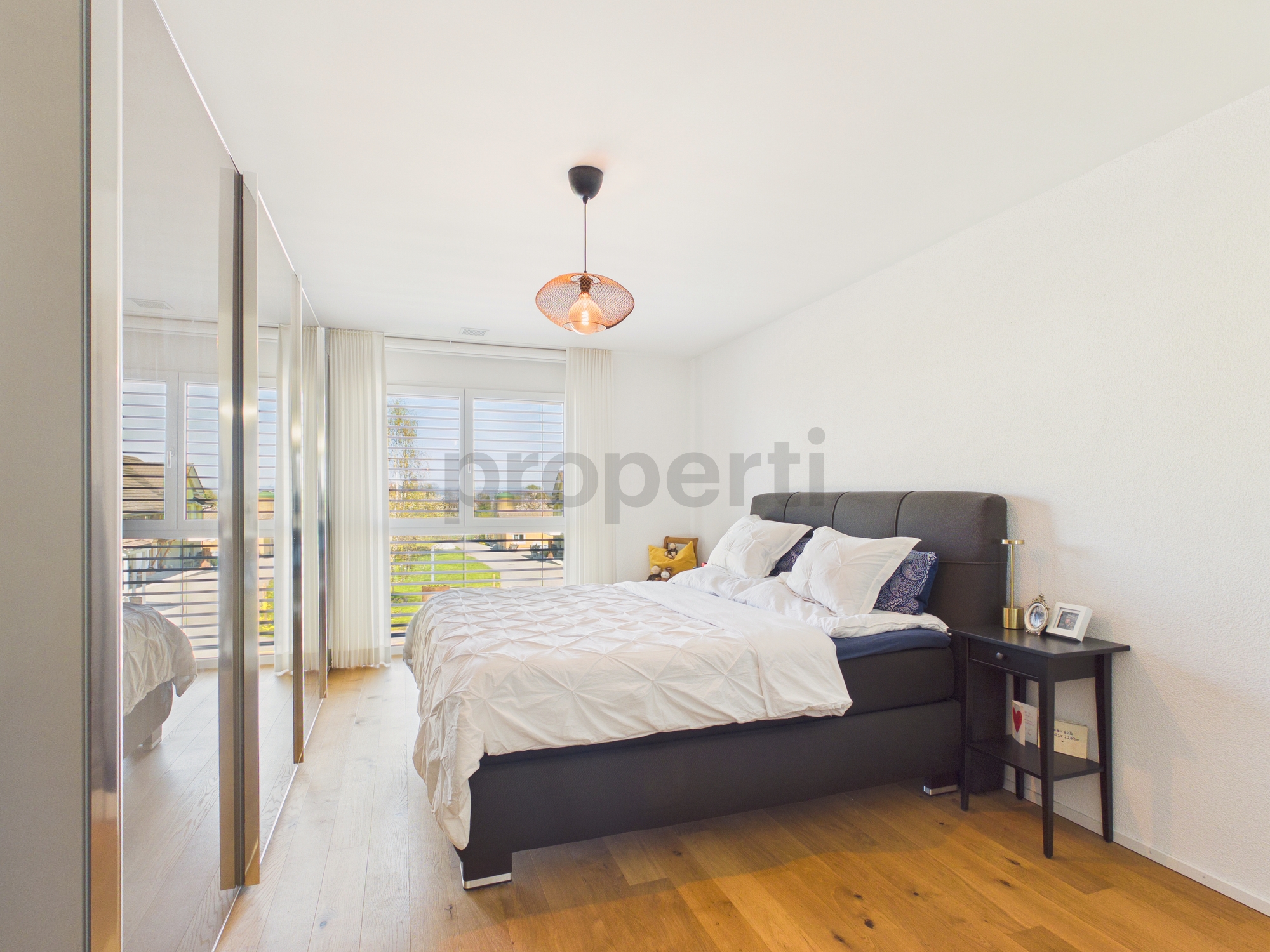 Helles Schlafzimmer mit großem Fenster und dunklem Bett