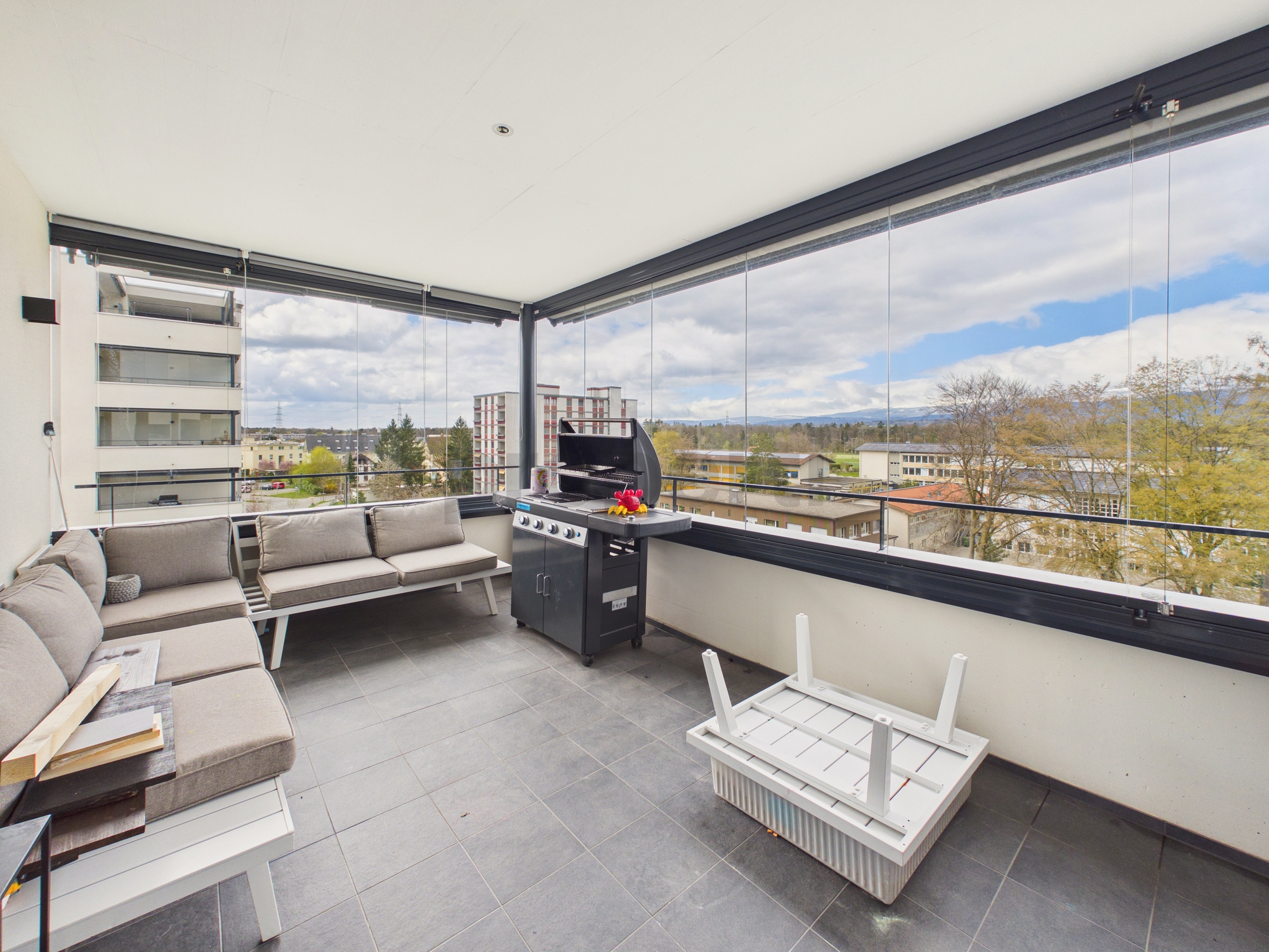 Großzügiger verglaster Balkon mit Sitzgruppe und Grill