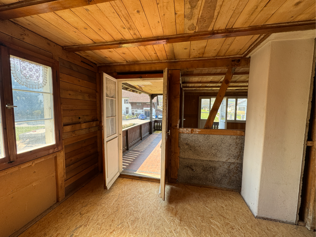Rustikaler, teils renovierungsbedürftiger Innenraum mit Holzausstattung und Balkontür