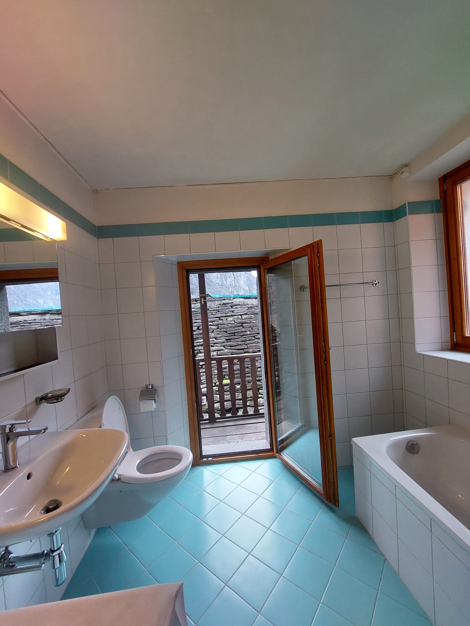 Badezimmer mit türkisfarbenem Fliesenboden und Zugang ins Freie