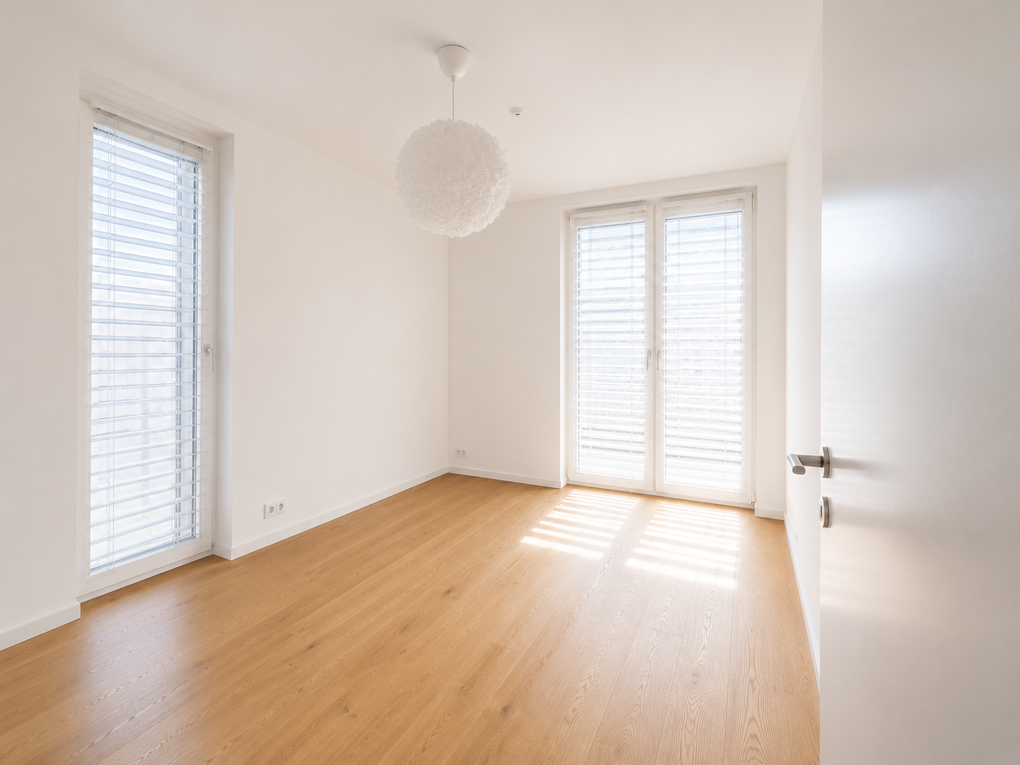 Helles, leeres Schlafzimmer mit Holzparkett und großen Fenstern