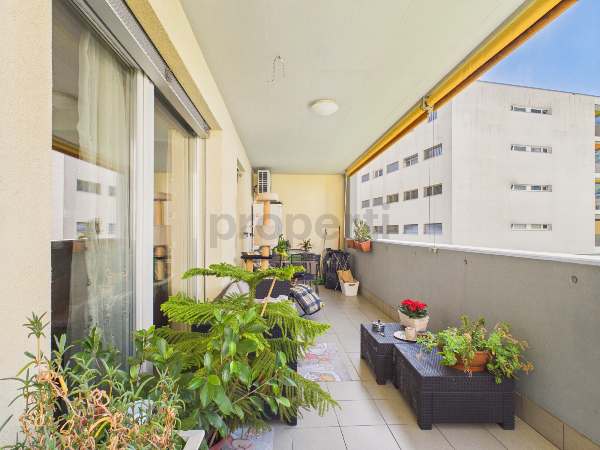 Überdachter Balkon mit Pflanzen und Sitzmöbeln