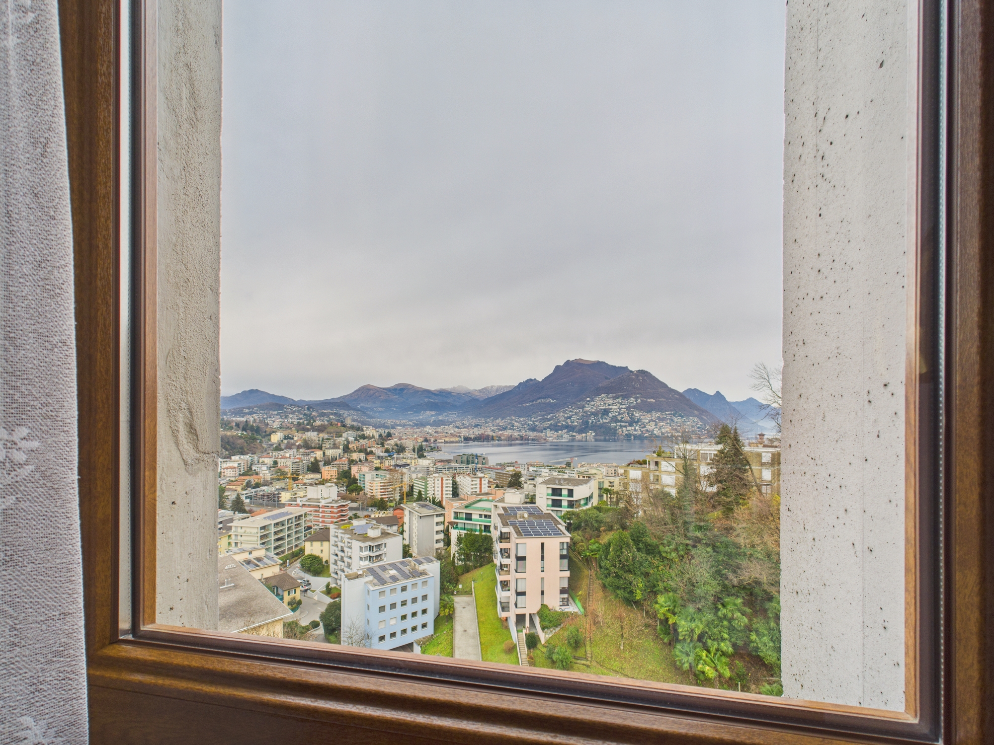 Ausblick durch ein Holzfenster auf Stadt, See und Berge