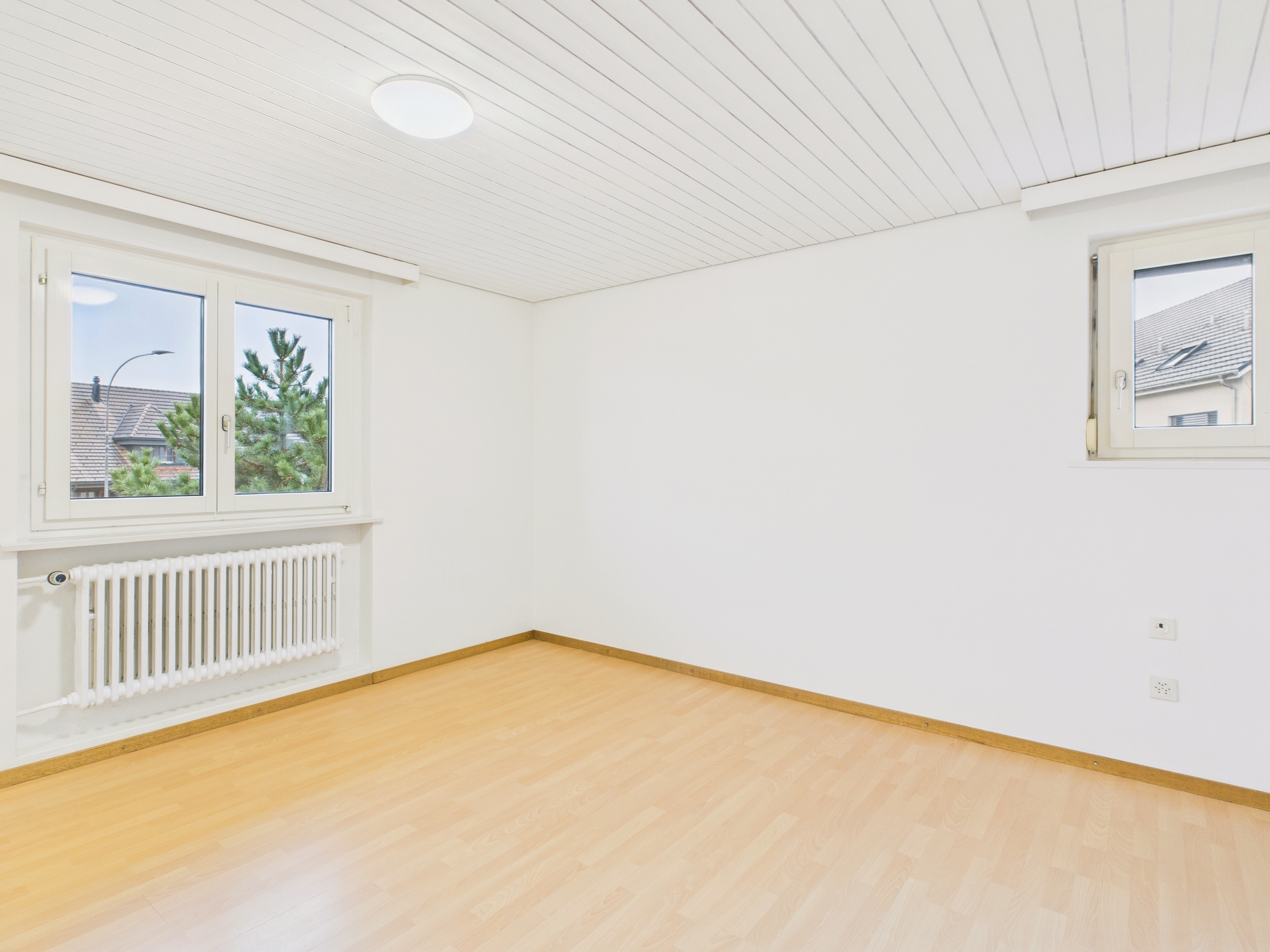 Helles, leeres Zimmer mit Fensterfront und Heizkörper