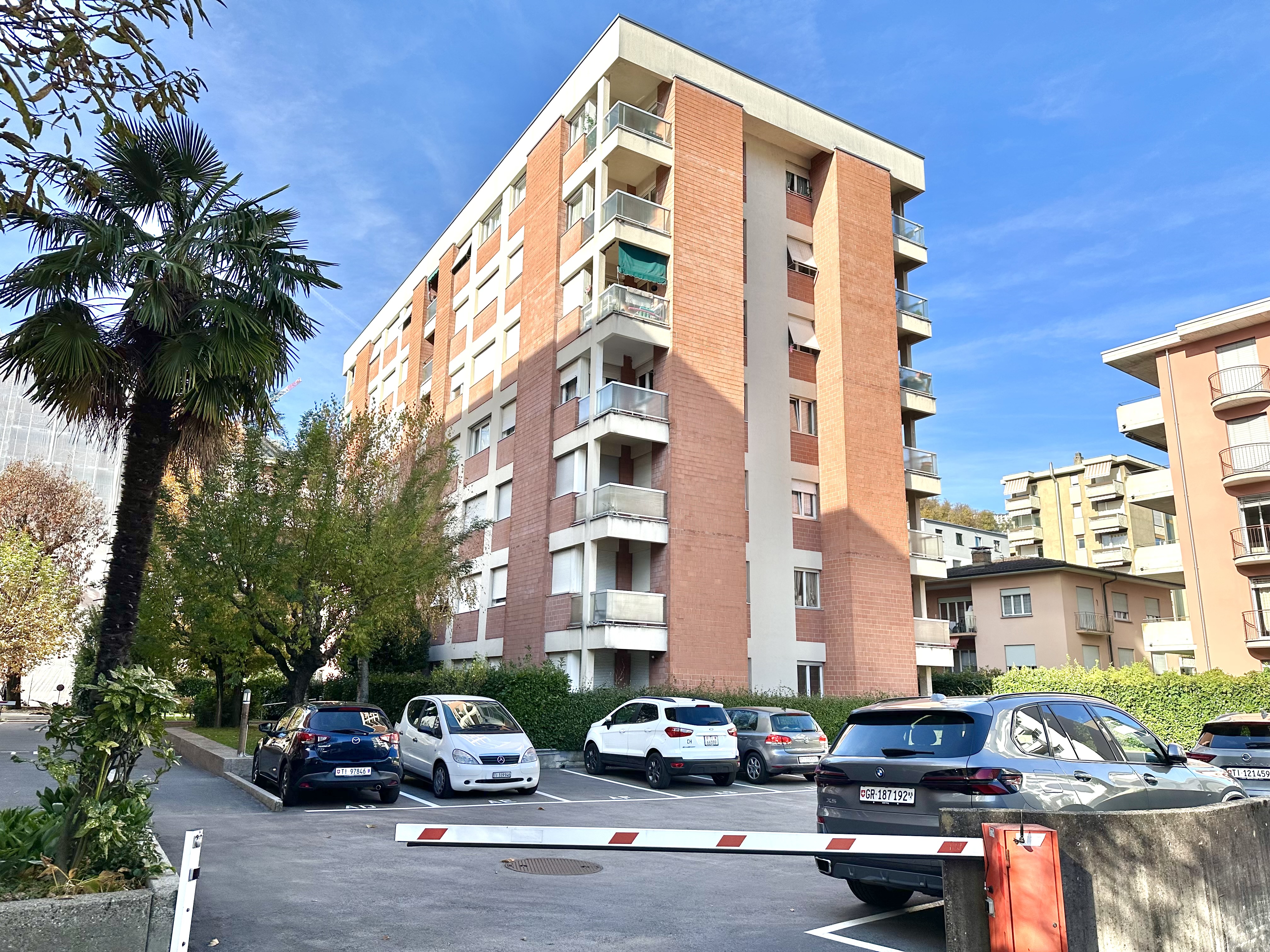 Mehrfamilienhaus mit Palmen und Parkplatz