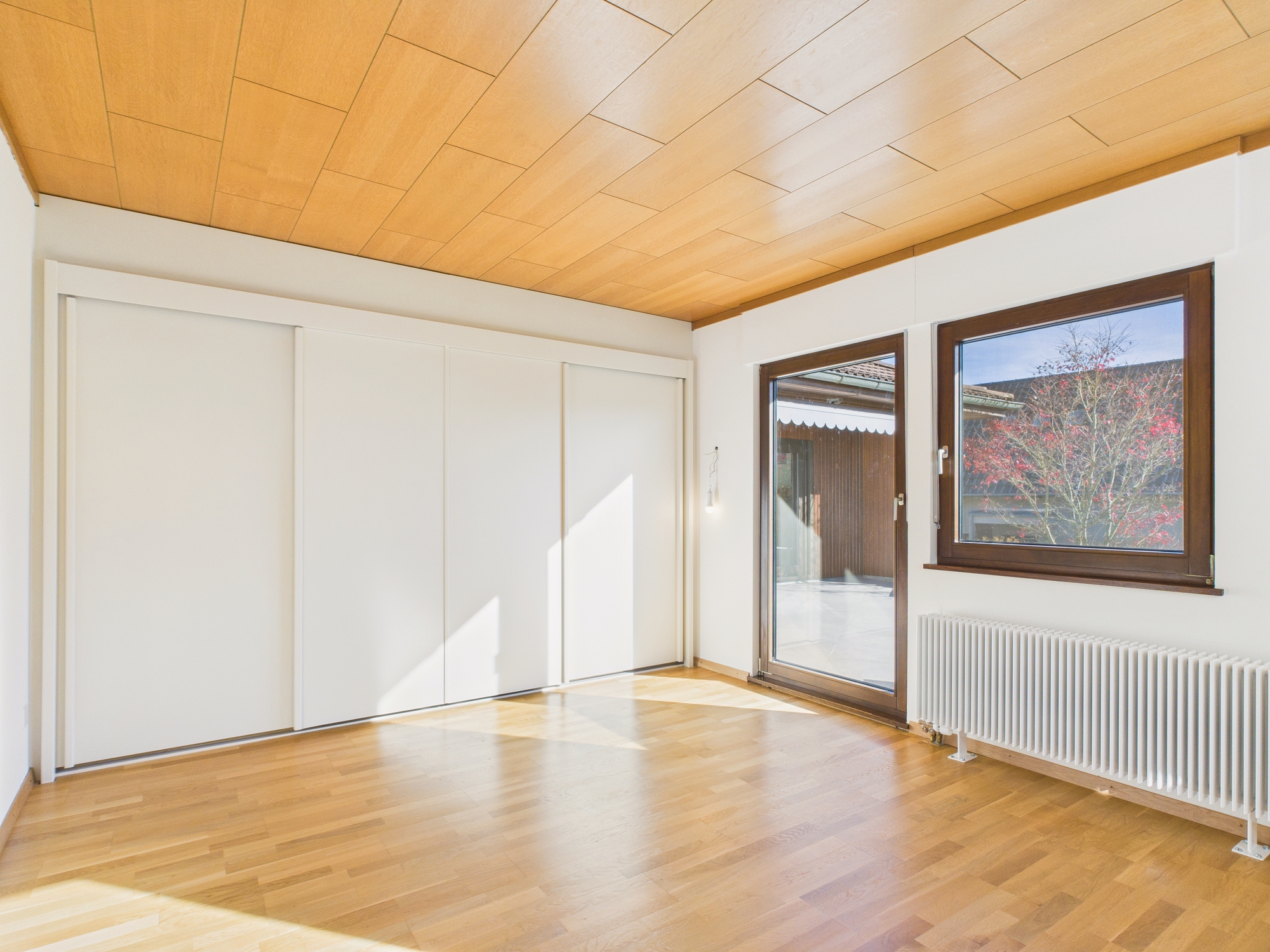 Heller, leerer Wohnraum mit Holzdecke und Fensterfront