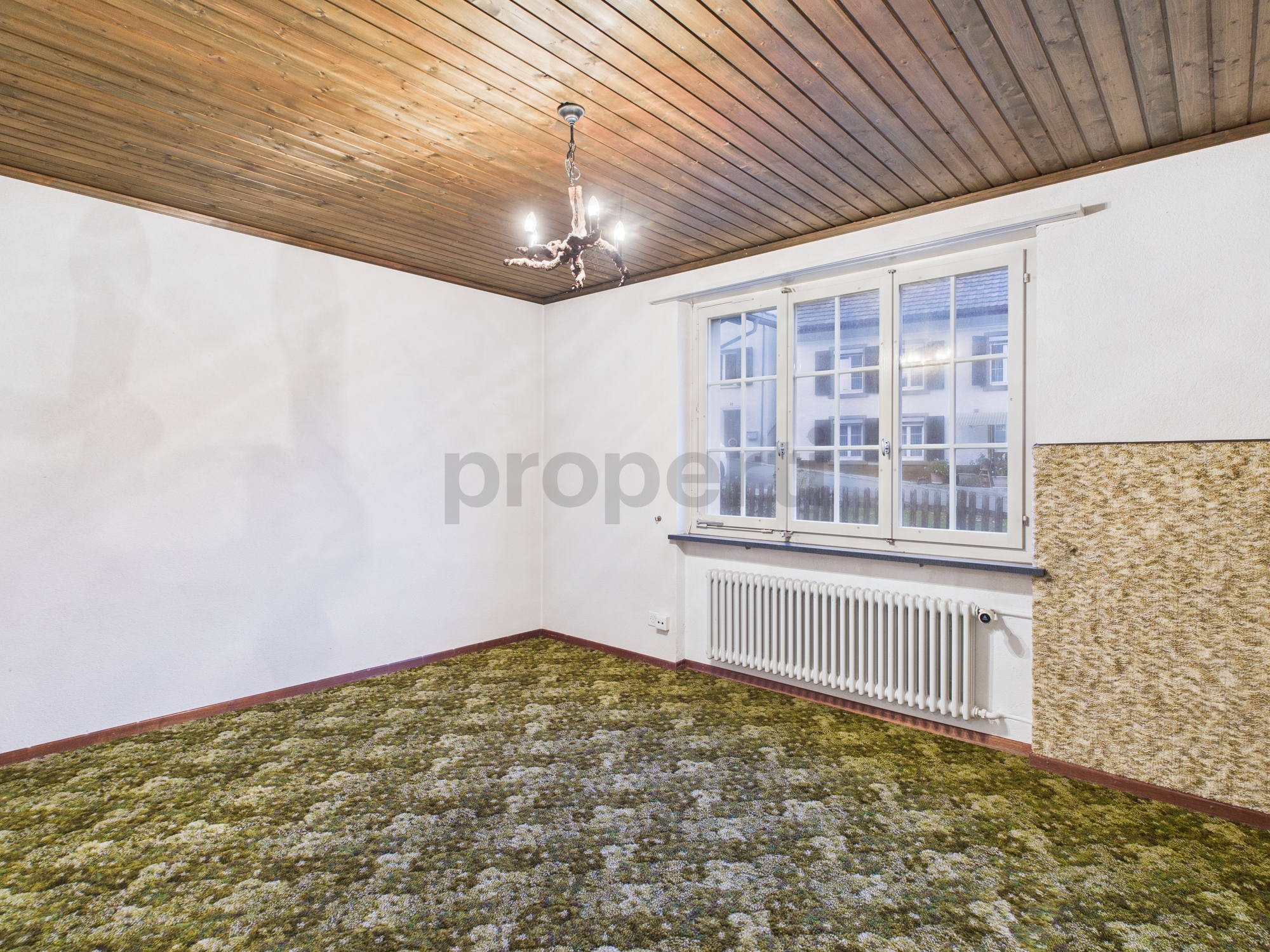 Leerer Wohnraum mit Holzdecke und grünem Teppich