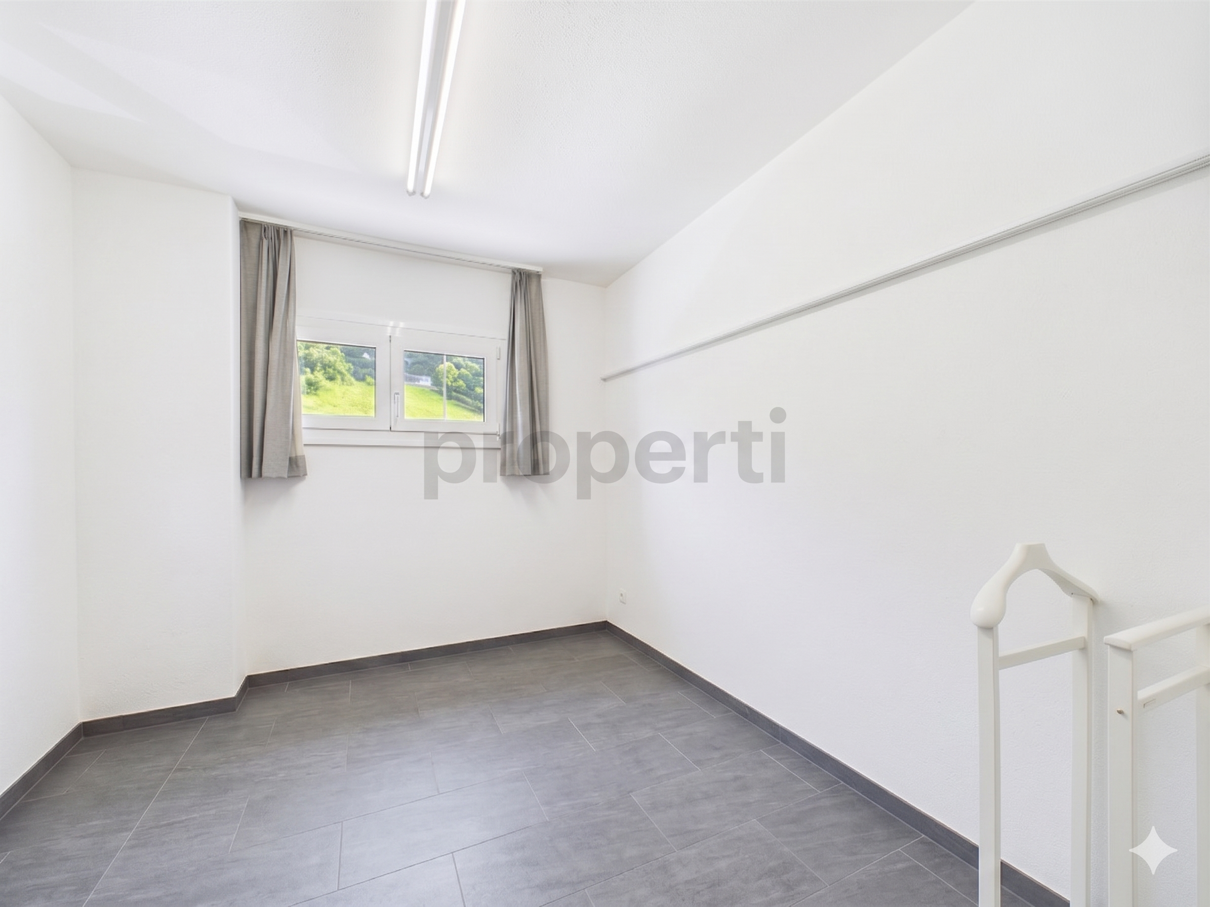 Helles, leeres Dachgeschosszimmer mit Fenster und Treppe