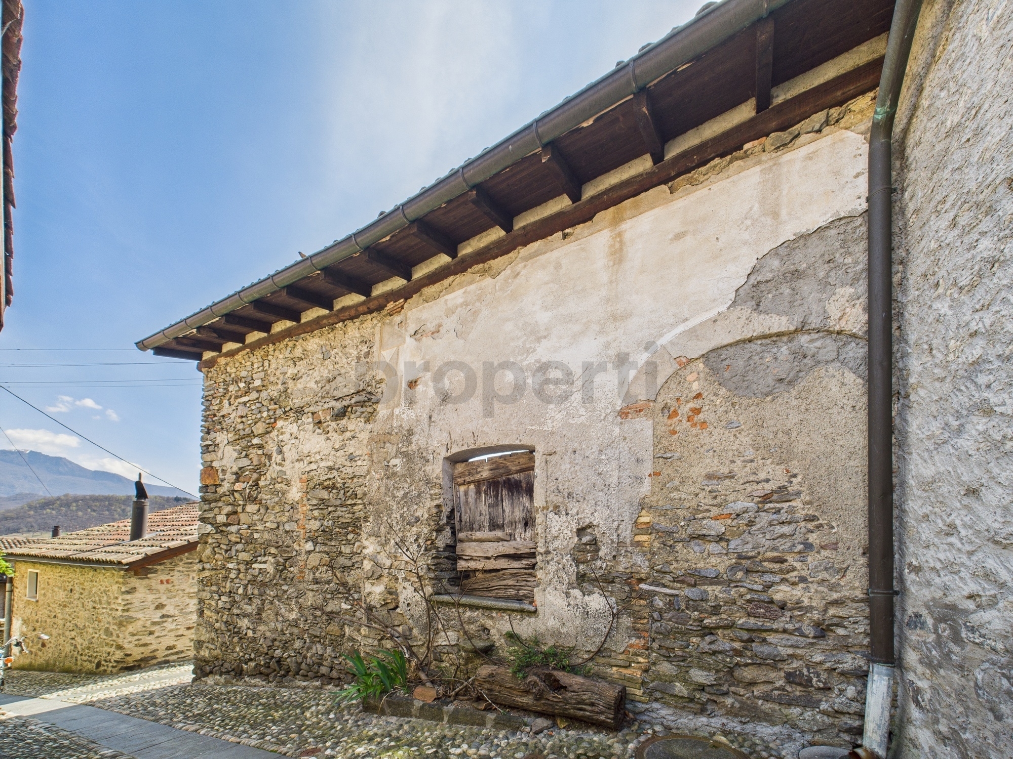 Alte Steinfassade mit verwittertem Putz und Blick ins Tal