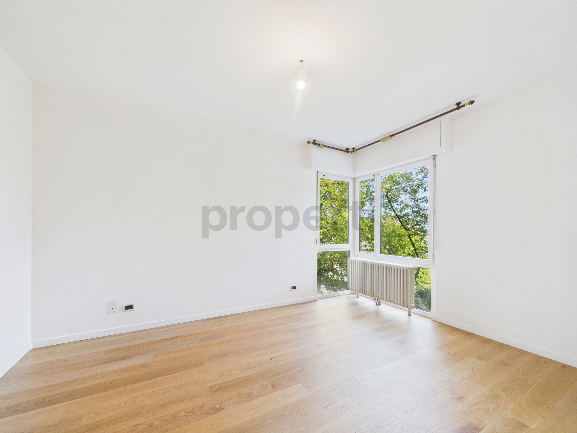 Helles leeres Zimmer mit Parkett und großem Eckfenster