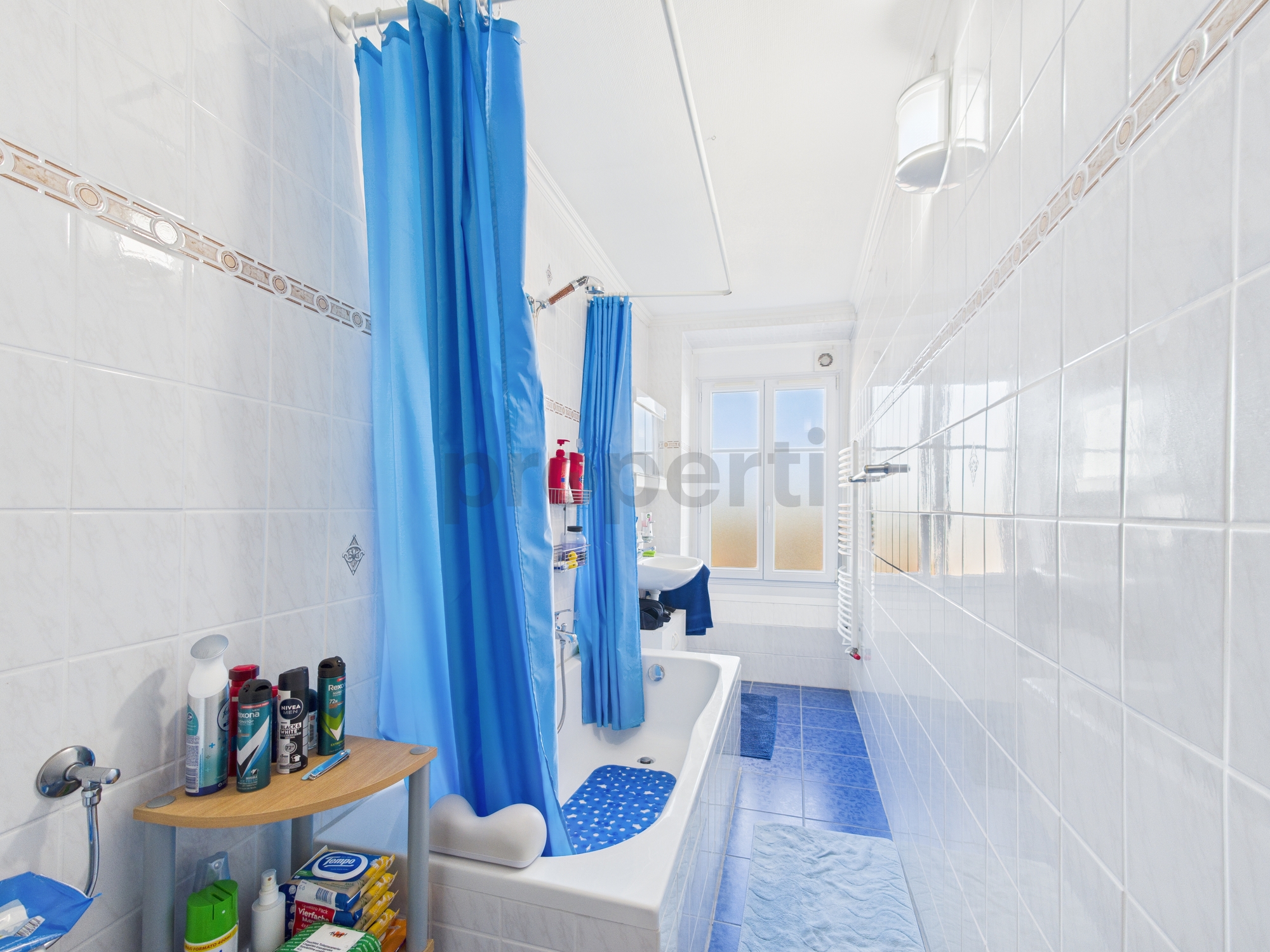 Helles schmales Badezimmer mit Badewanne und blauen Vorhängen