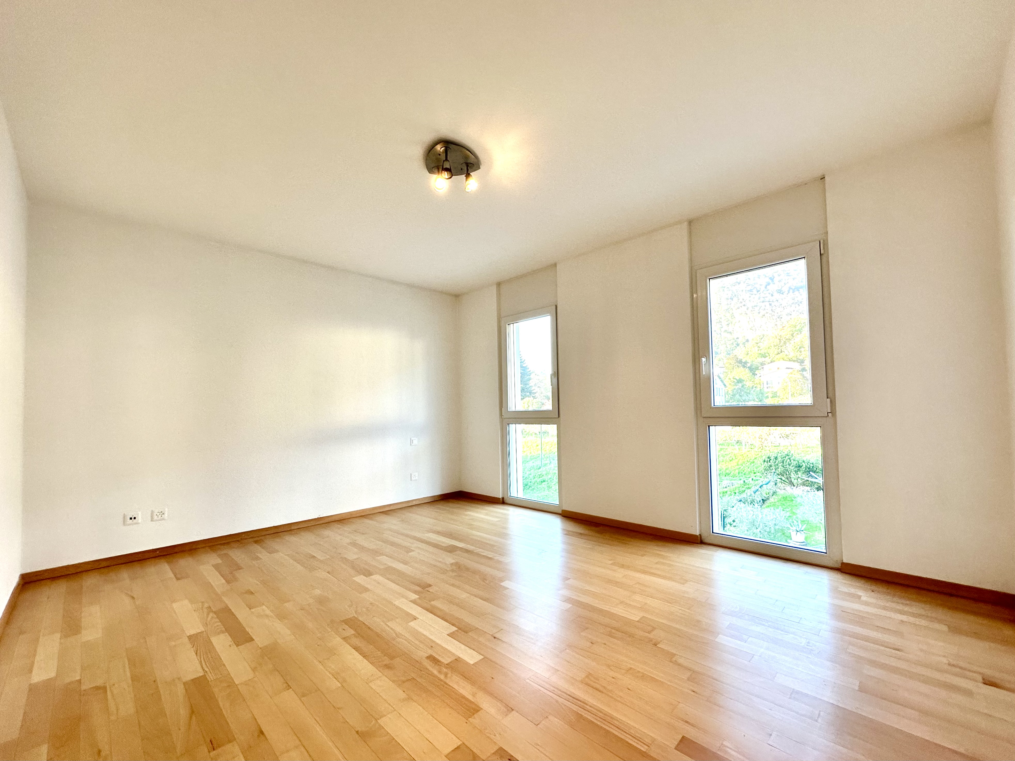 Helles, leeres Zimmer mit Parkett und hohen Fenstern
