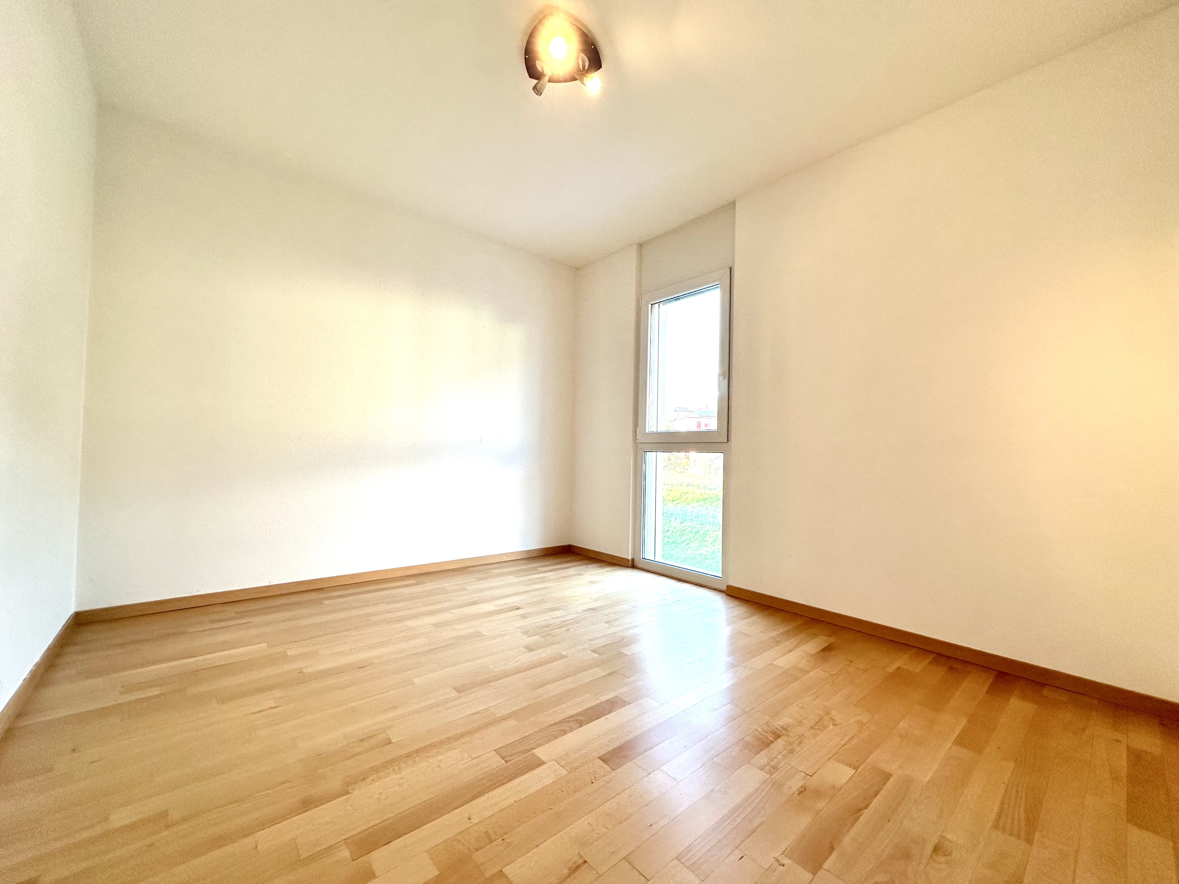 Heller leerer Raum mit Holzparkett und hohem Fenster