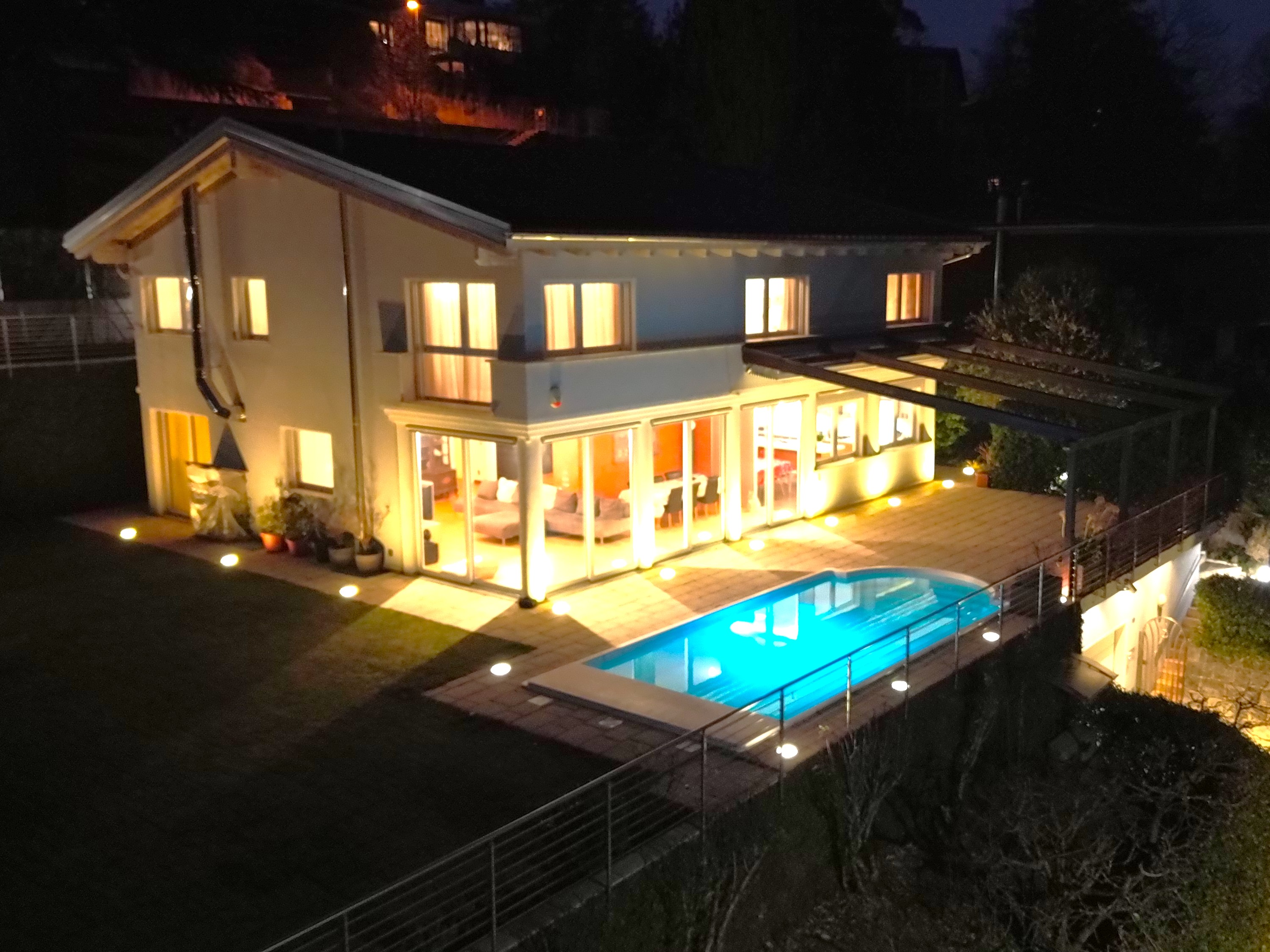 Außenansicht eines modern beleuchteten Einfamilienhauses mit Pool