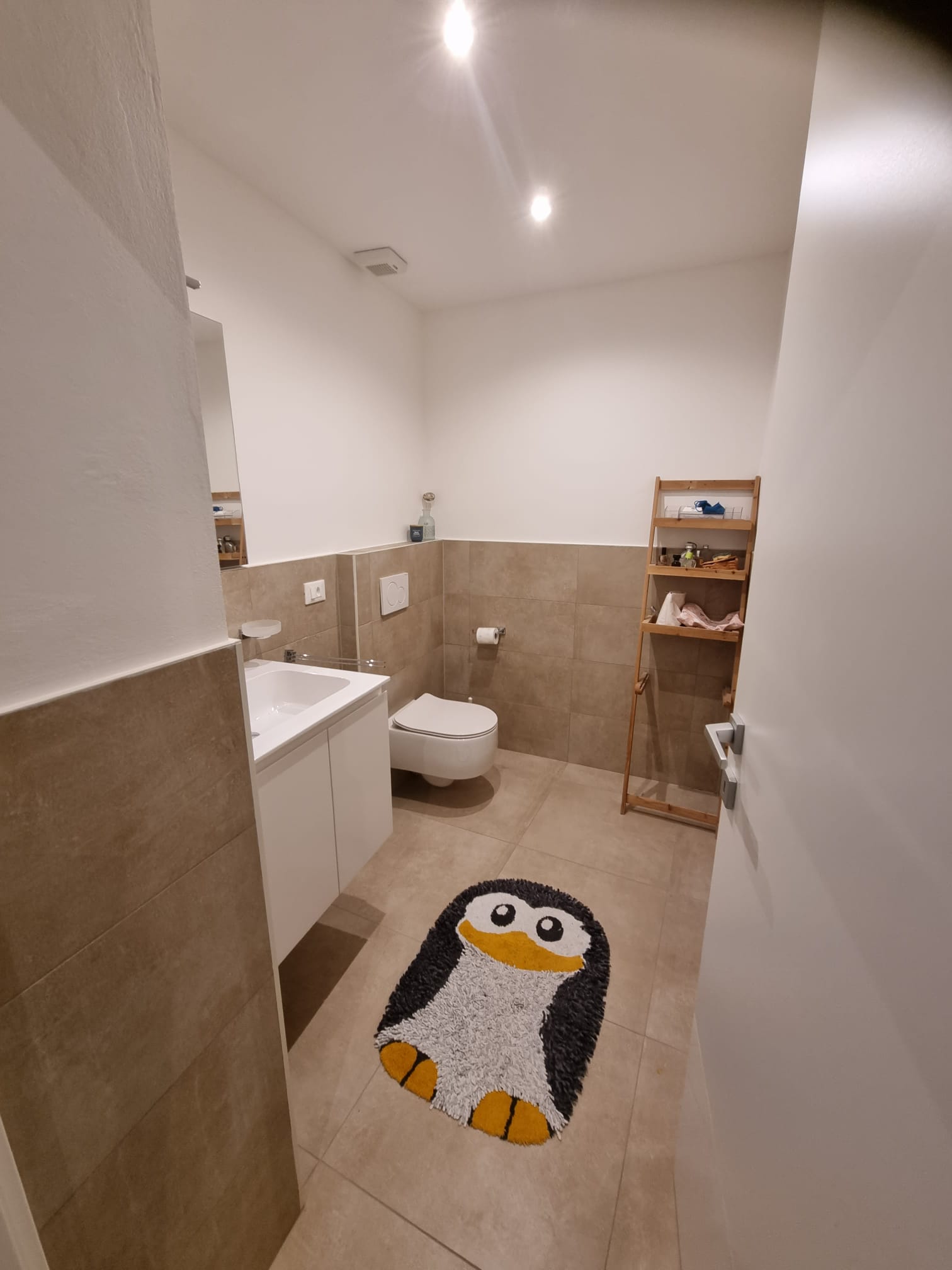 Modernes Gäste-WC mit warmen Fliesen und Pinguin-Teppich