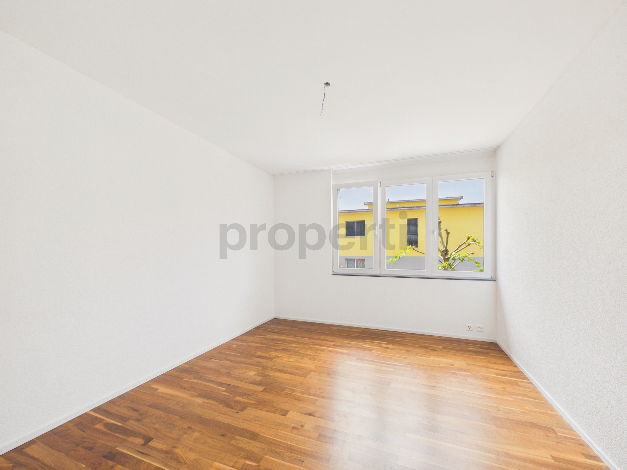 Leerer heller Raum mit Parkettboden und Fenster