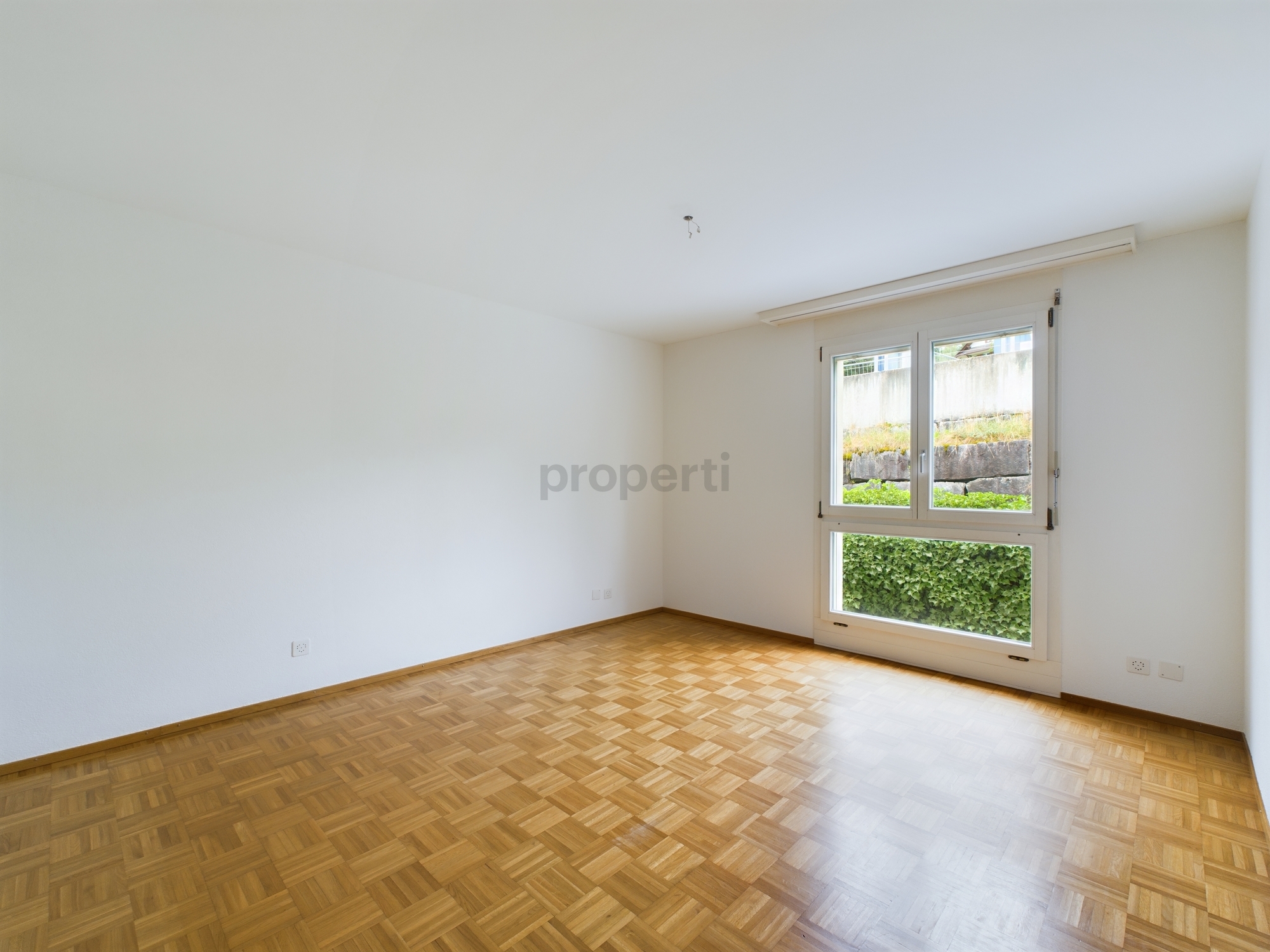 Leerer heller Raum mit Parkettboden und großem Fenster