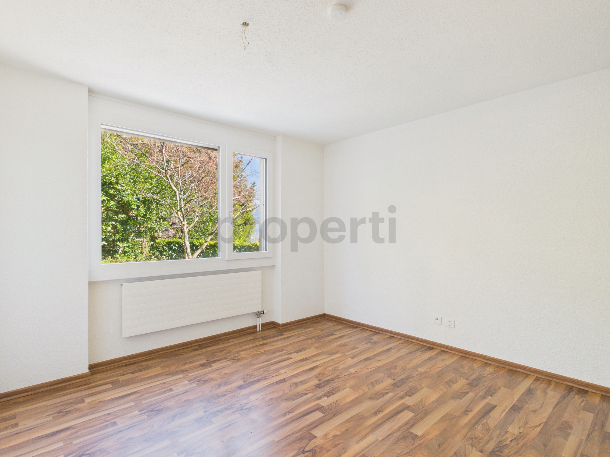 Leerer, helles Zimmer mit Fenster und Holzoptik-Boden