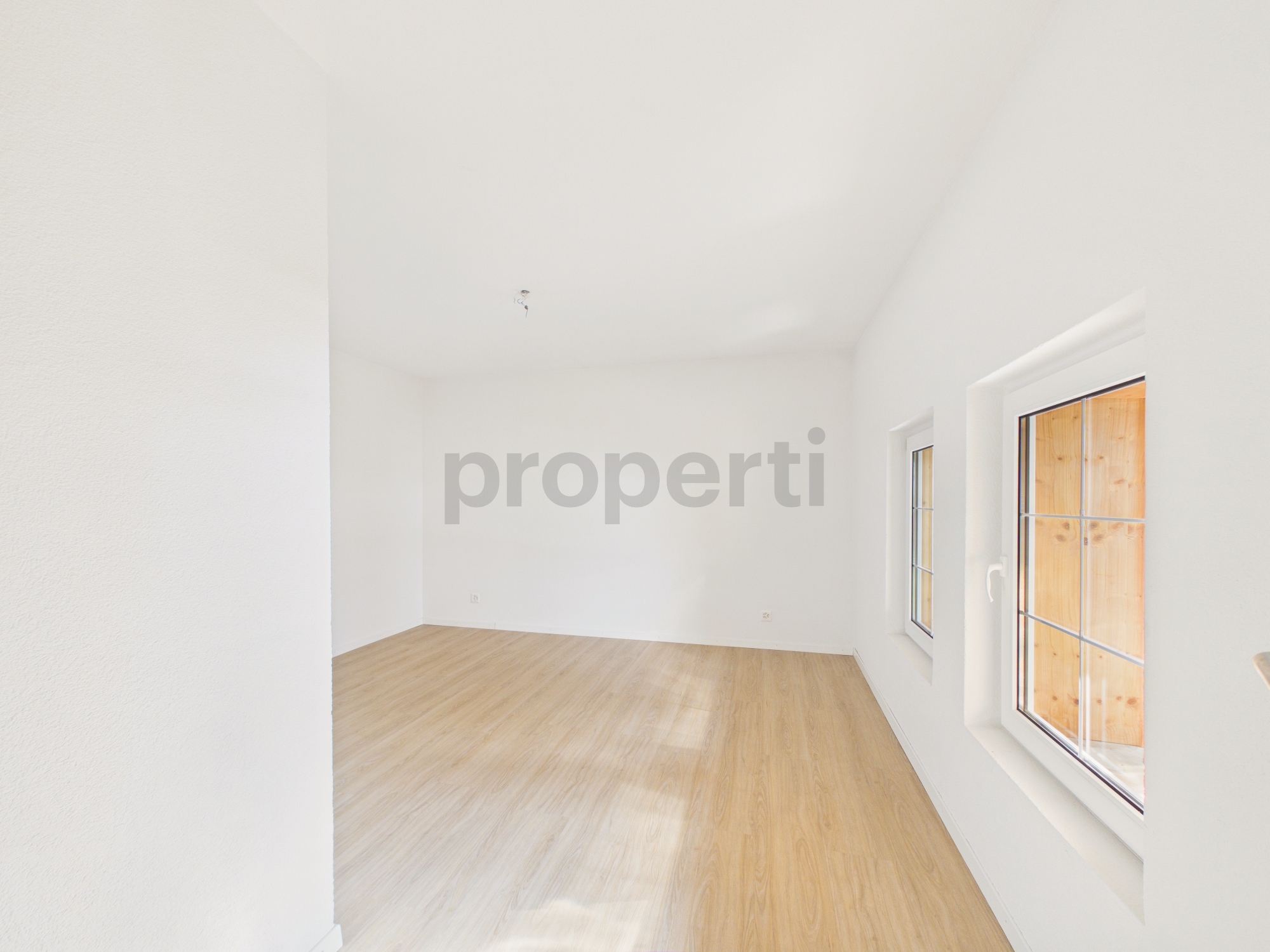 Heller leerer Raum mit Holzoptikboden und Fenstern