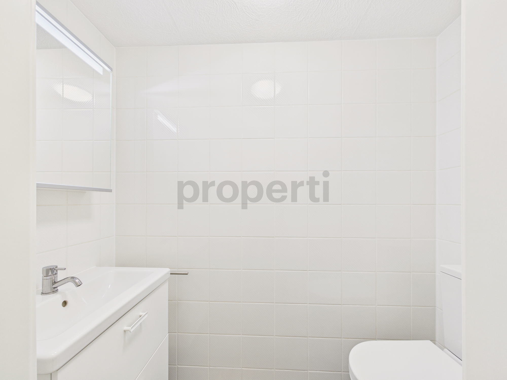 Kleines weißes Badezimmer mit Waschbecken und WC