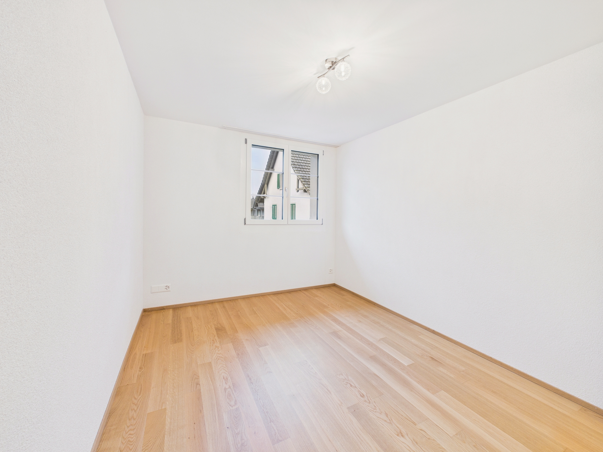 Helles, leeres Zimmer mit Parkettboden und Fenster