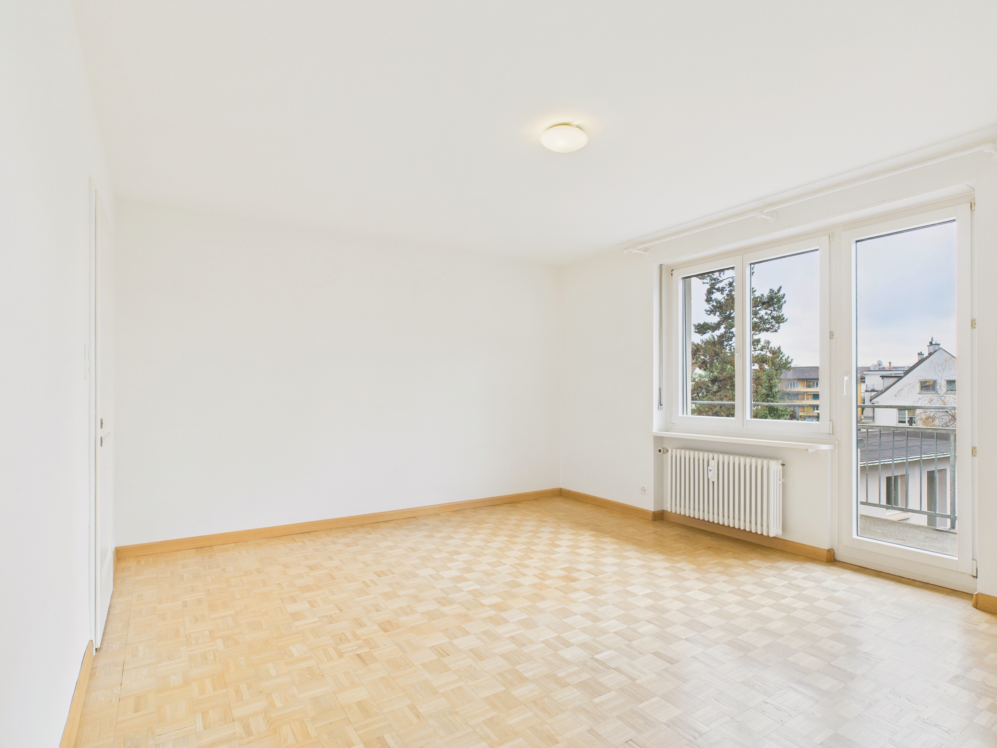 Heller leerer Raum mit Parkett und Balkonfenster