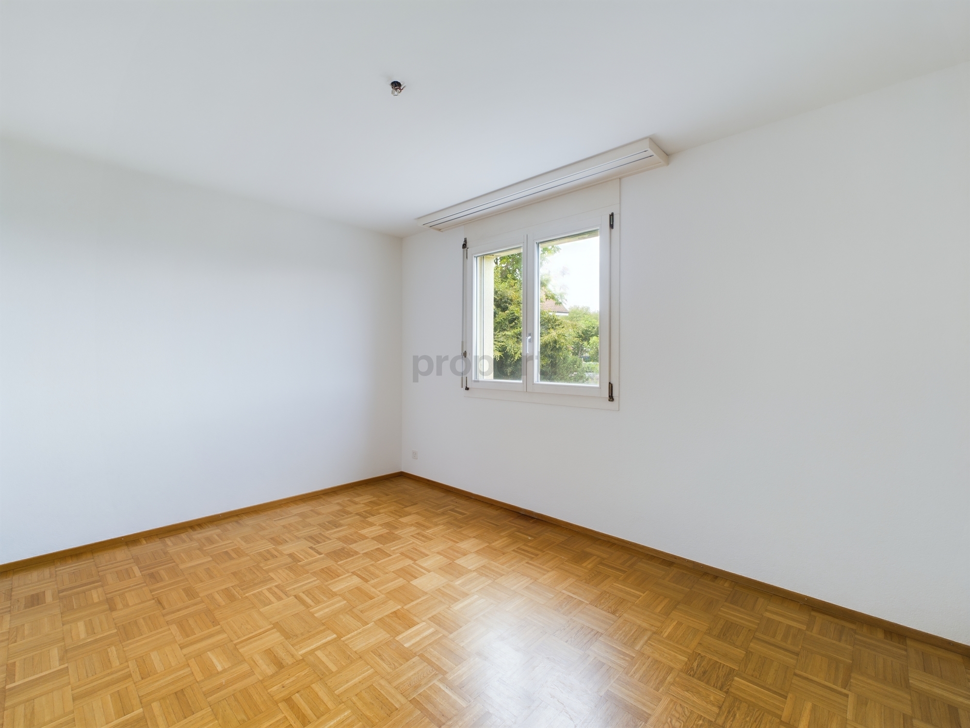 Leerer heller Raum mit Parkettboden und Fenster