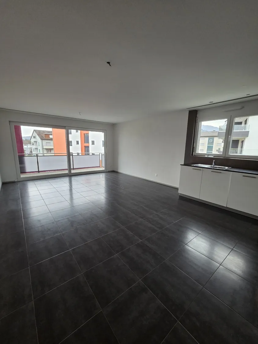 Großer leerer Wohnbereich mit Balkon und Küchenzeile