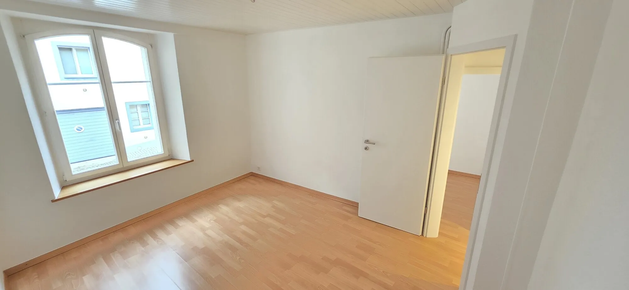 Helles, leeres Zimmer mit Holzfußboden und Fenster