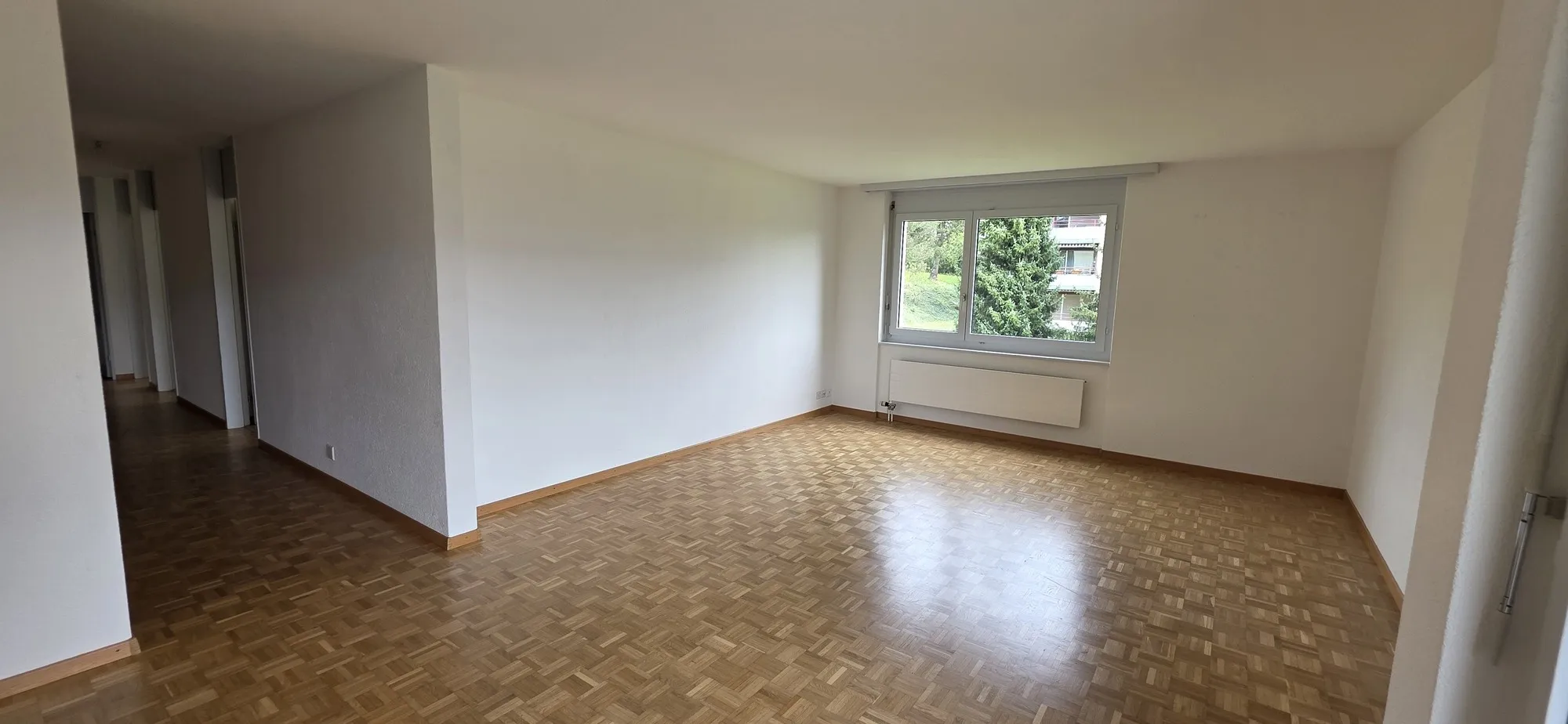 Leeres Wohnzimmer mit Parkettboden und Fensterblick